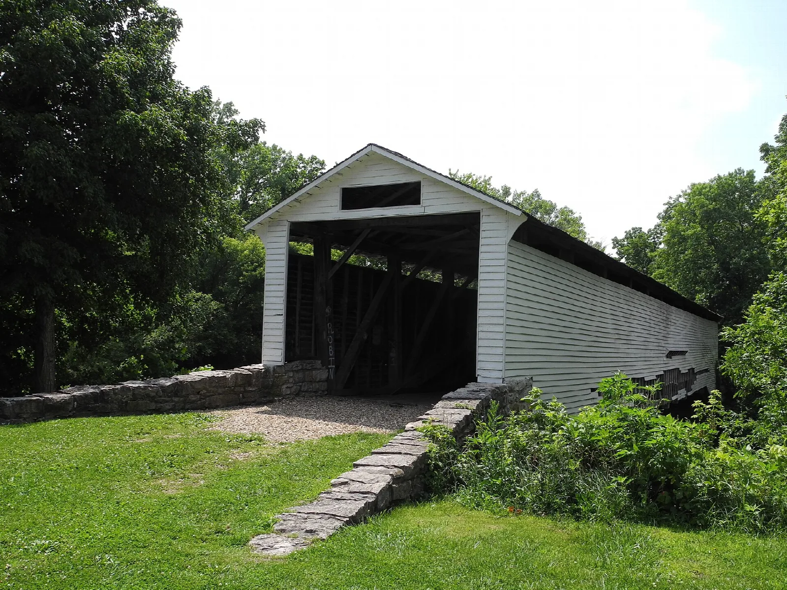 White covered bridge entrance with a stone path, framed by trees