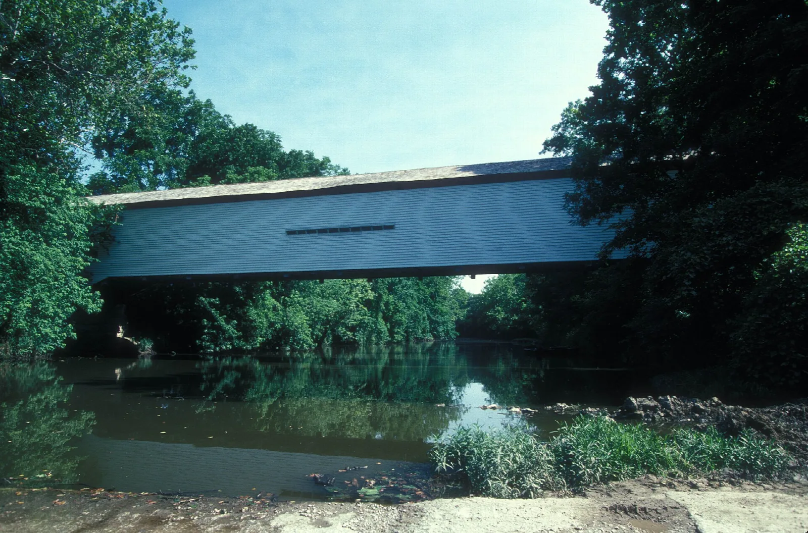 Long covered bridge over a river reflecting green trees