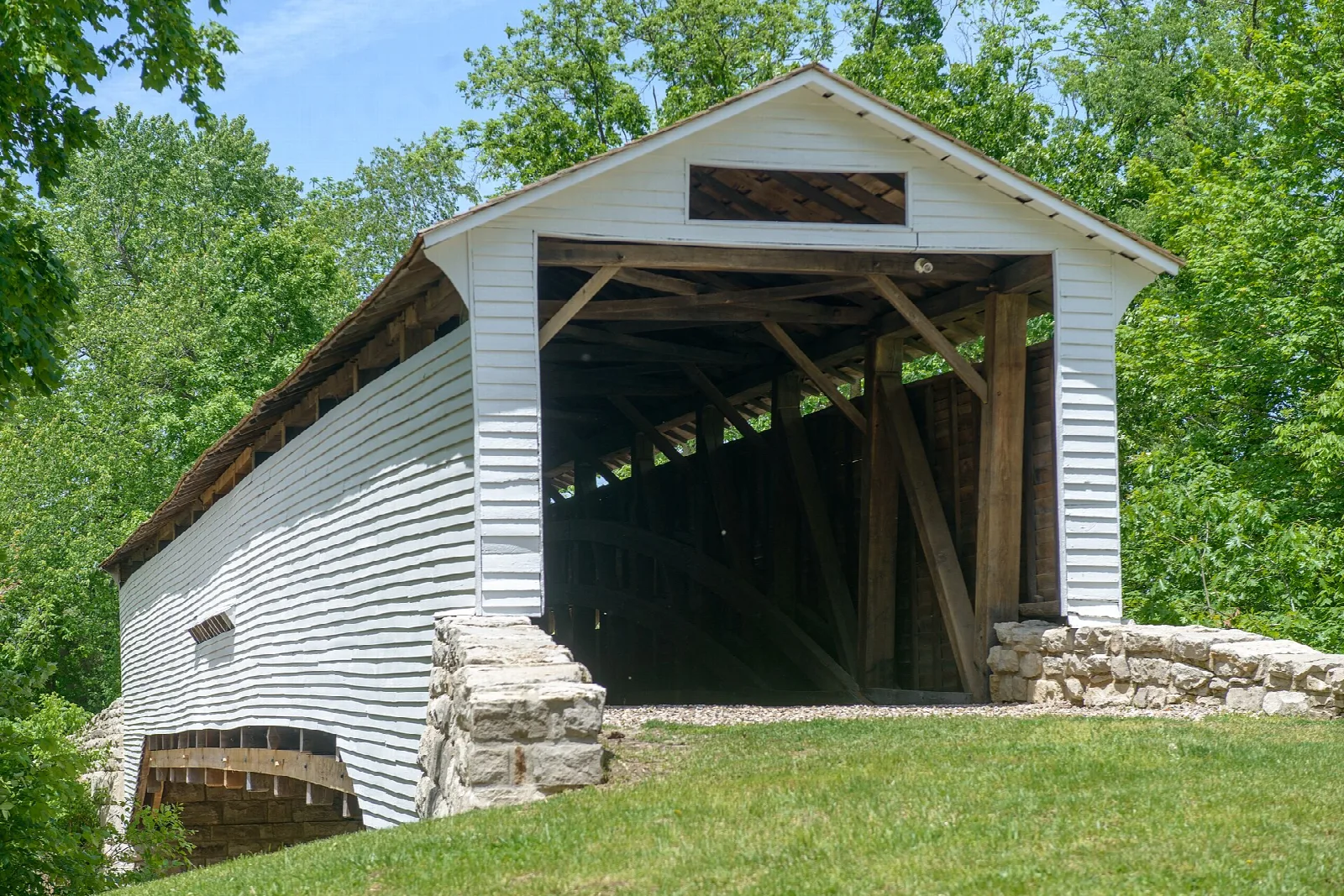 White covered bridge with a wide open portal, seen from the side beside a stone wall