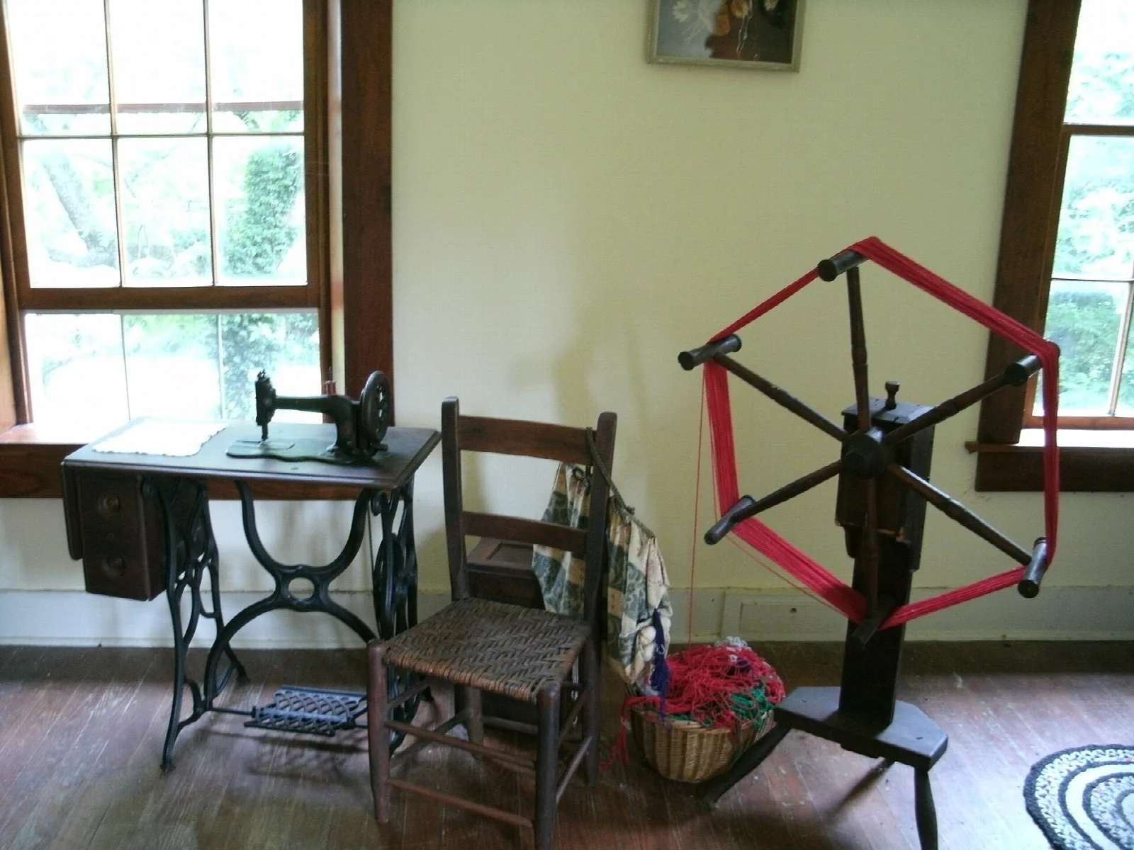 Room with a sewing machine, chair and a spinning wheel by two windows