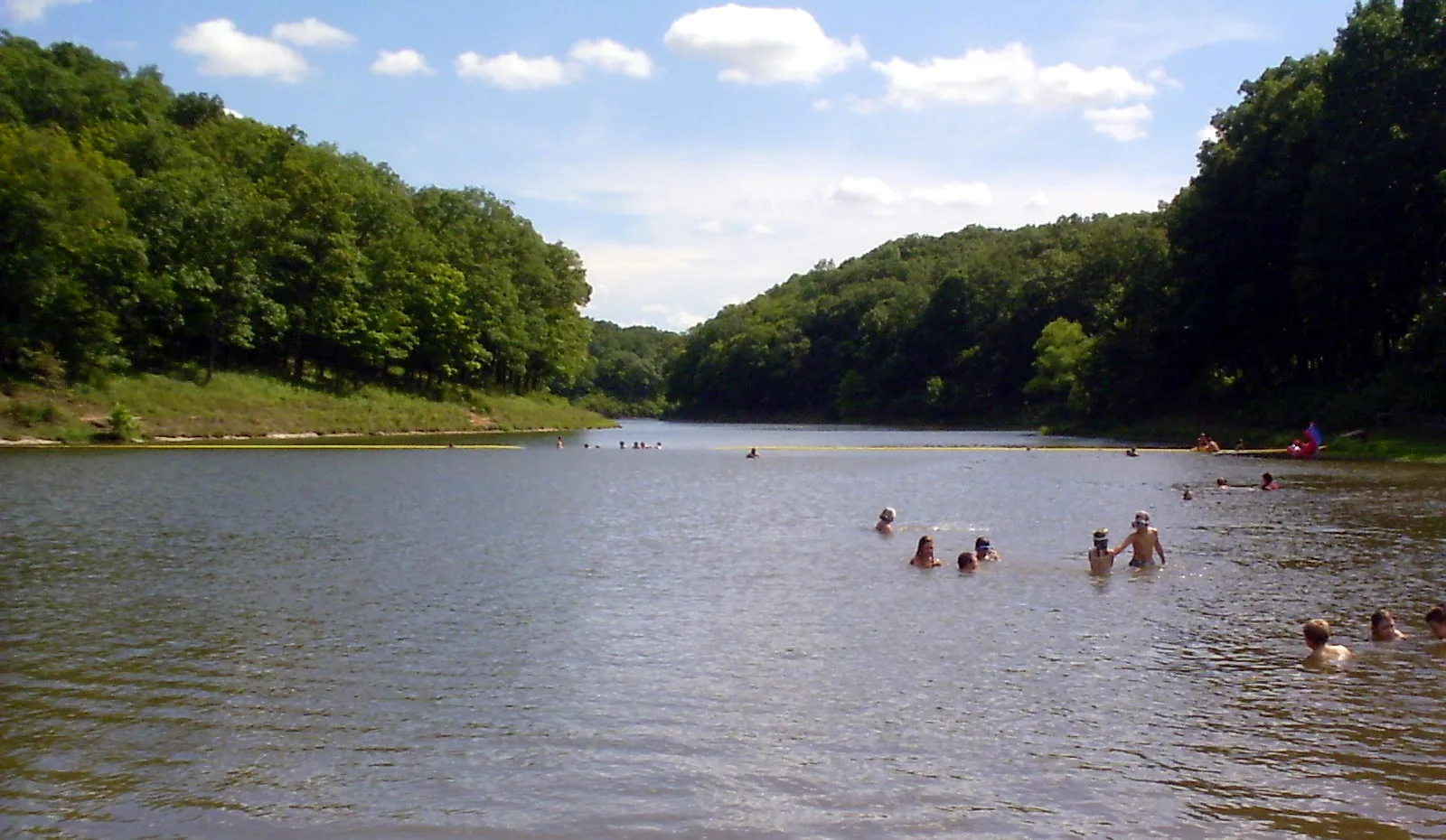 Swimmers in a lake ringed by green wooded hills