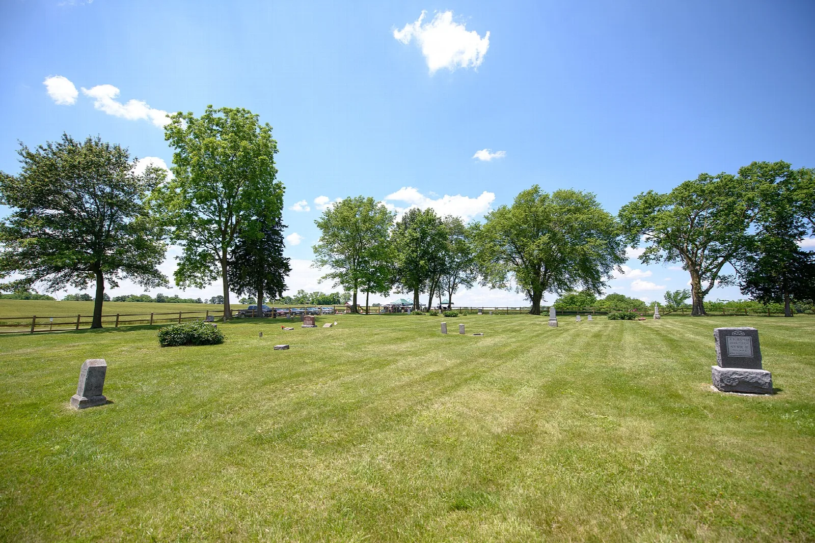 Mowed lawn with a few headstones and trees under a blue sky