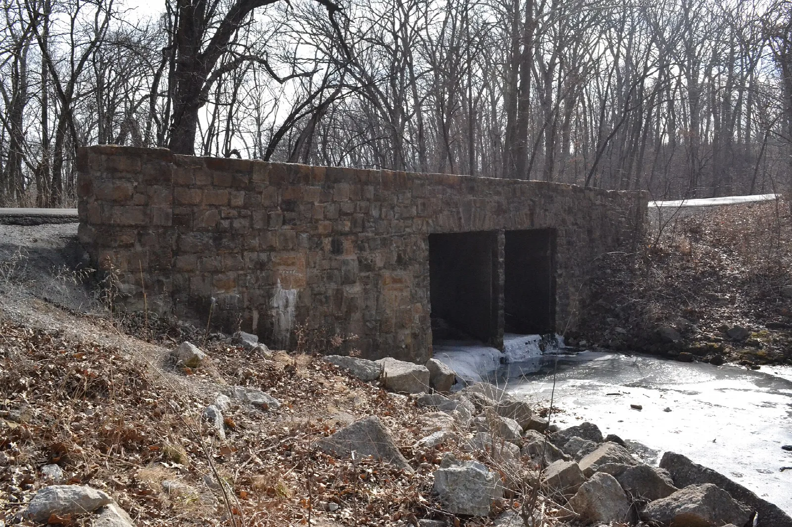 Stone bridge with two openings over a small creek among bare trees