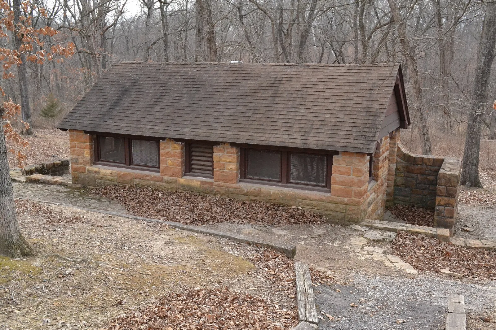 Low stone bath house with a brown roof among bare trees