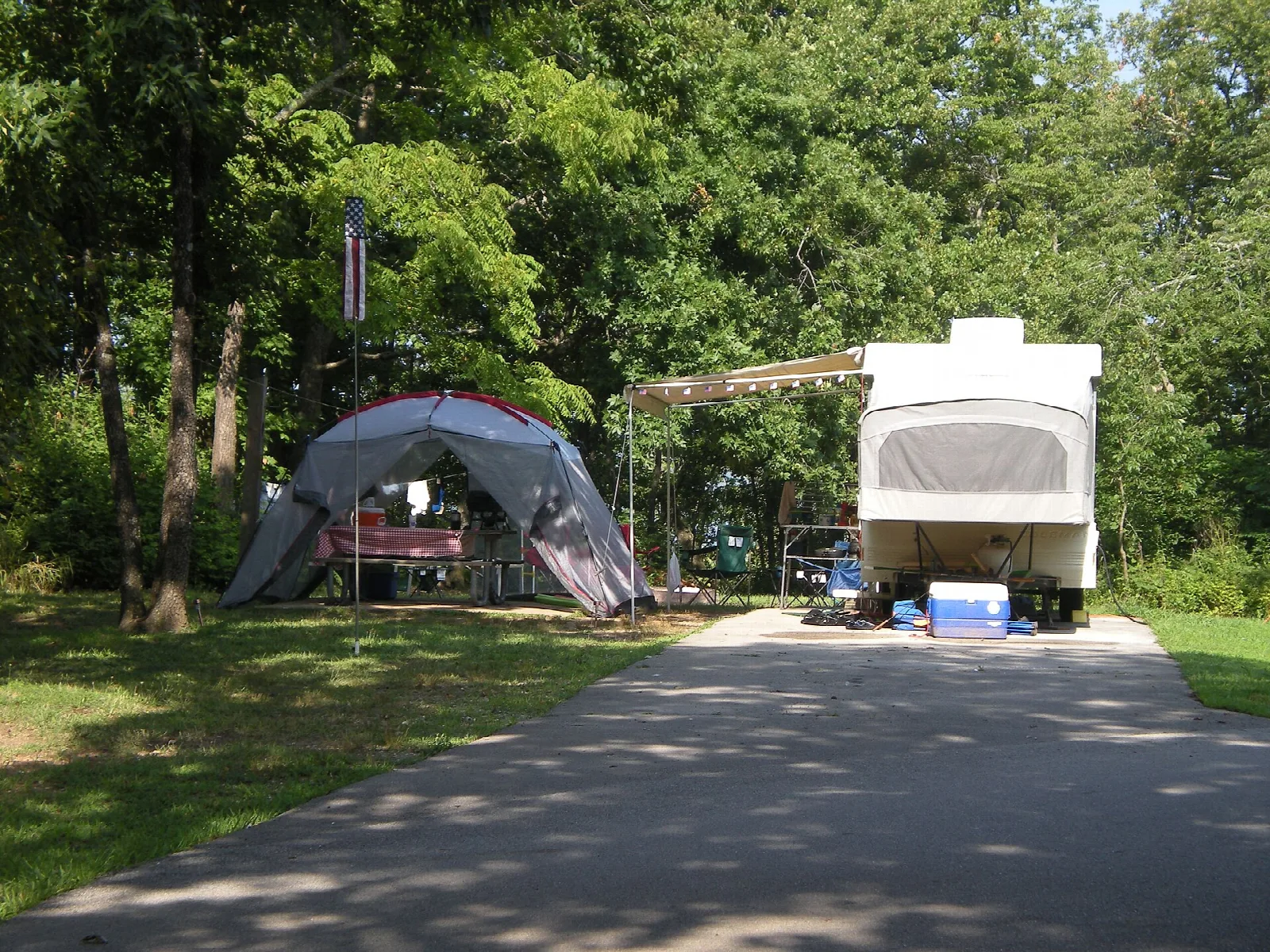 Paved campsite with a camper trailer and a tent among shady trees