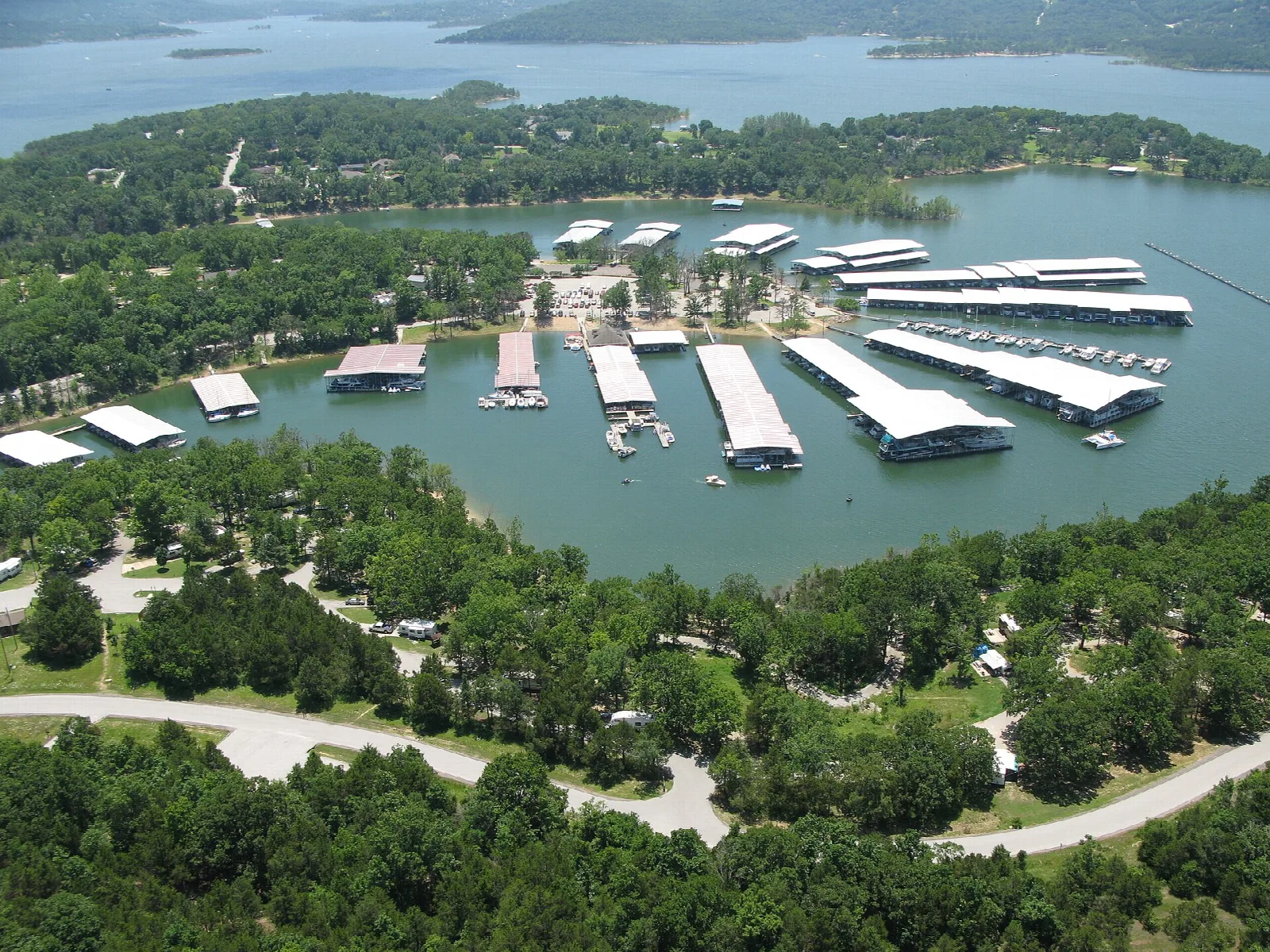 Aerial view of a marina with covered boat docks on a wooded lake shore