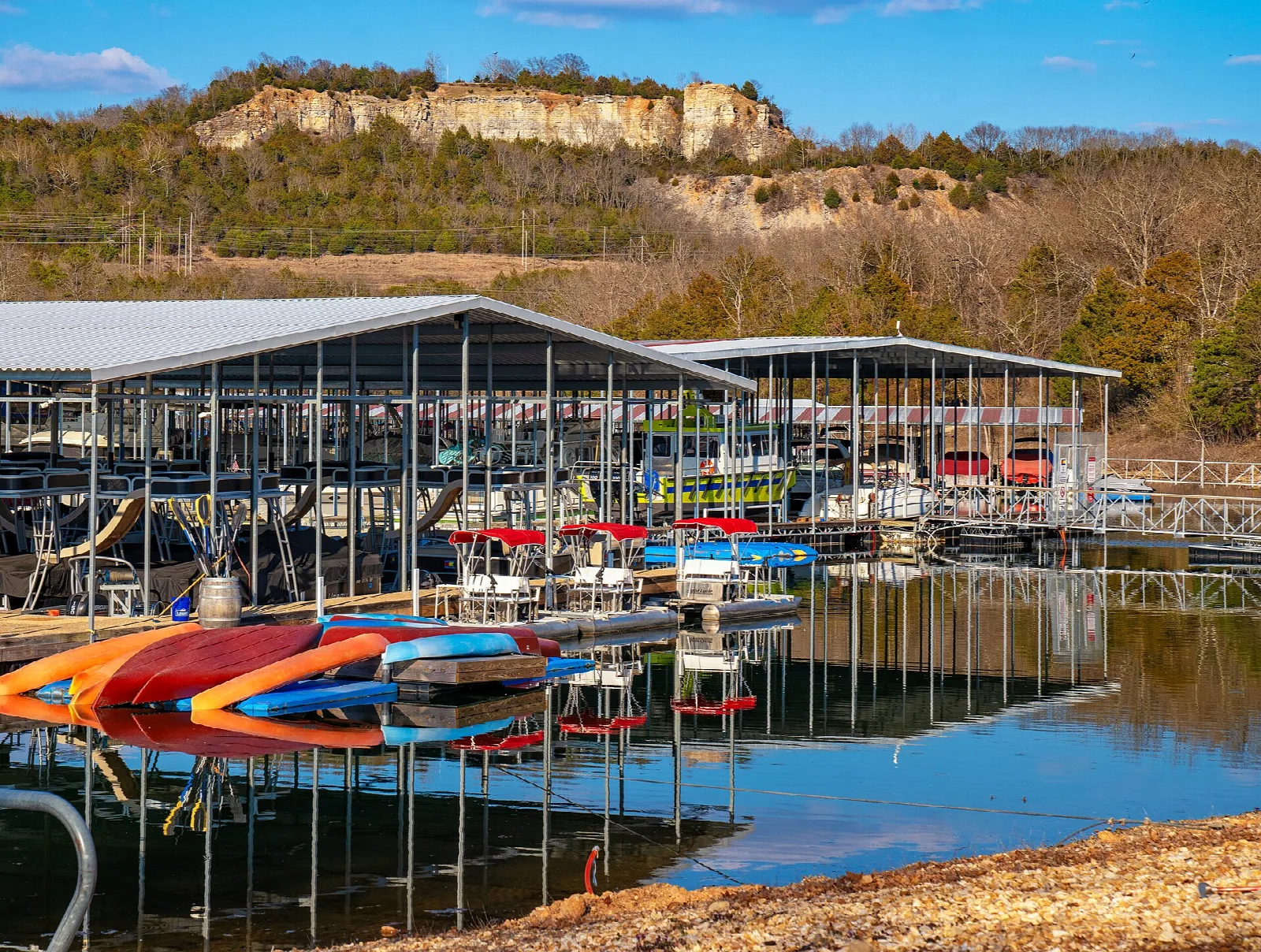 Covered boat docks with colorful kayaks below a rocky bluff on the lake