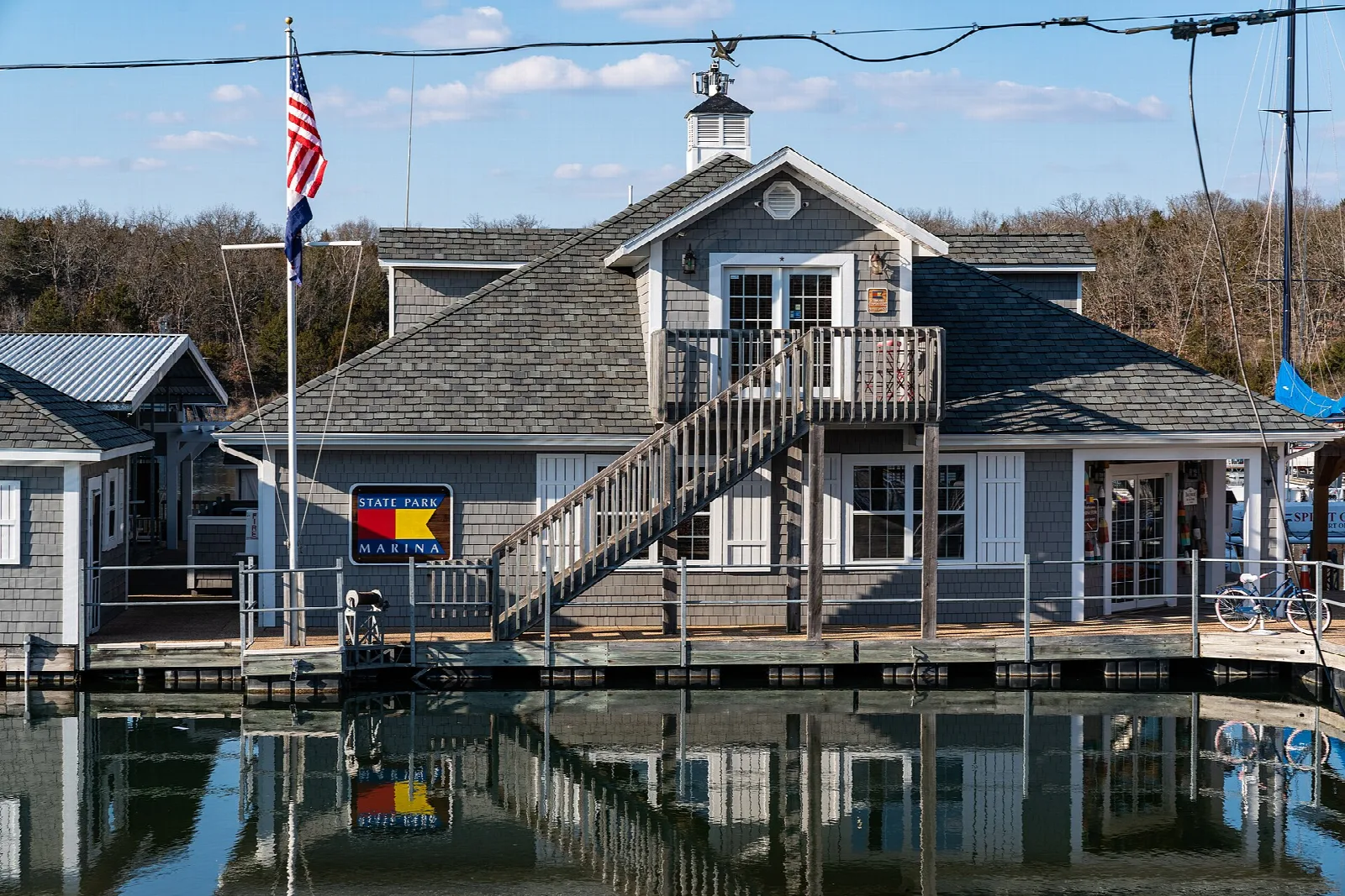 Gray lakeside marina building with a flag, reflected in calm water
