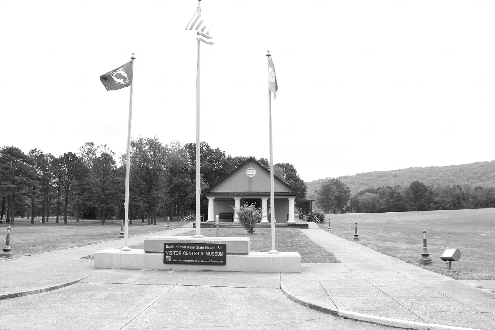 Pavilion with flagpoles in front, hills in the background, in black and white