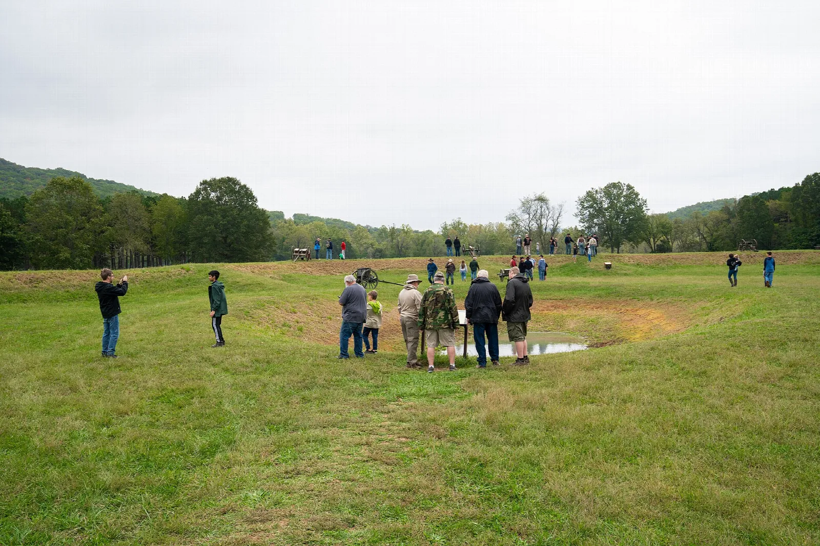 Visitors walking across a grassy fort earthwork with hills behind