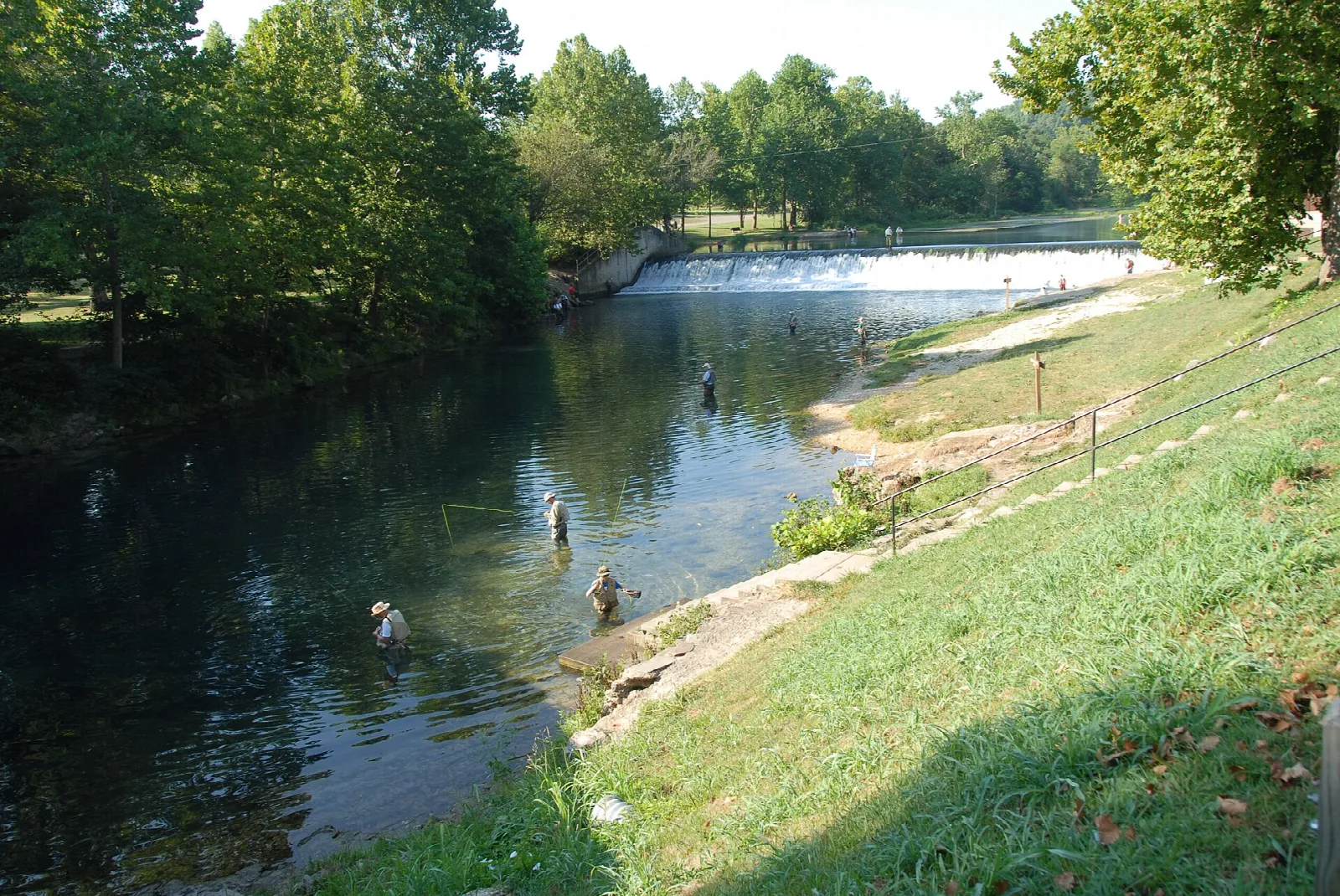 Anglers wading in a clear stream below a small dam