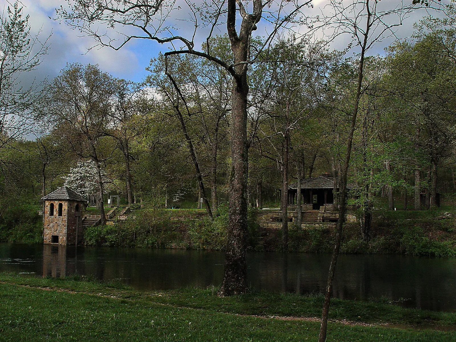 Small stone building and a shelter beside still water among trees