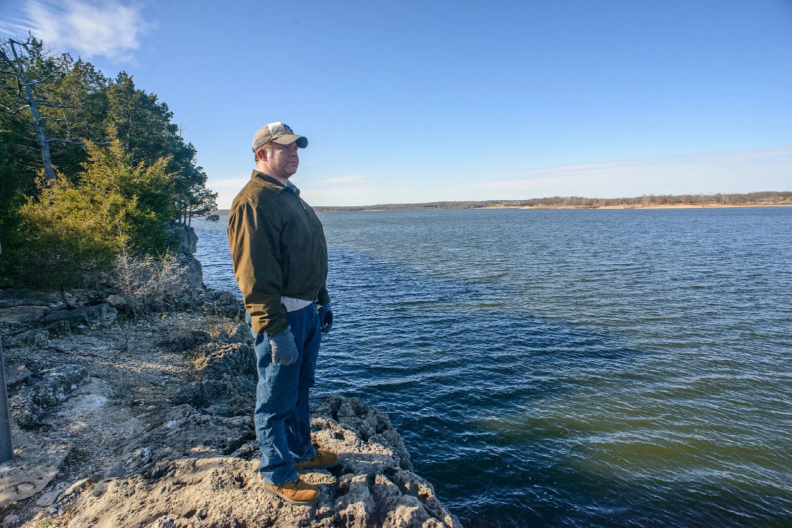 A person standing on a rocky ledge looking over a wide lake