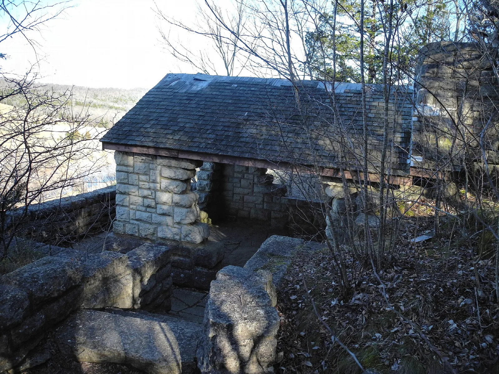 Stone shelter with a shingled roof at a hilltop overlook