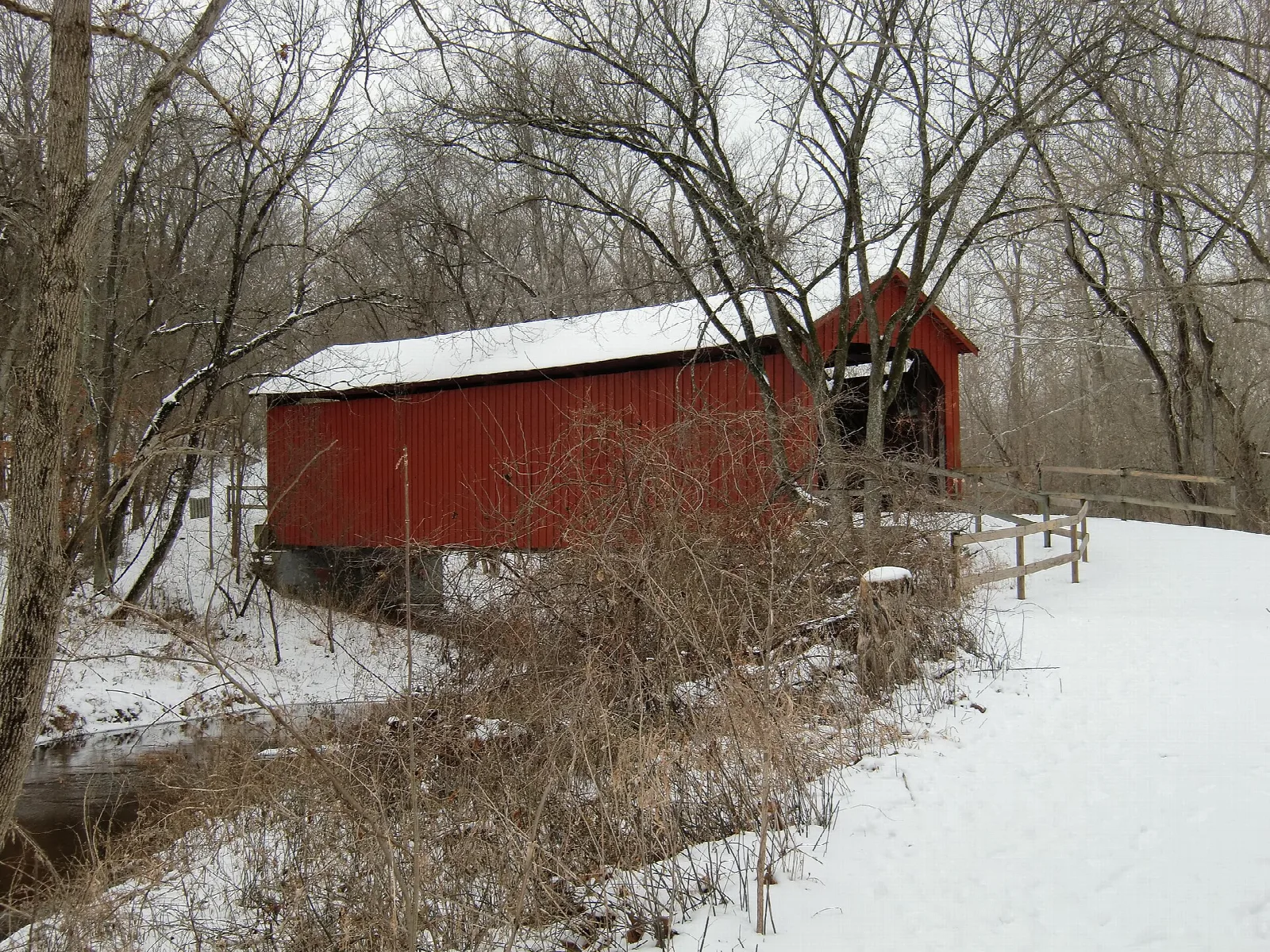 Red covered bridge beside a snowy path and creek