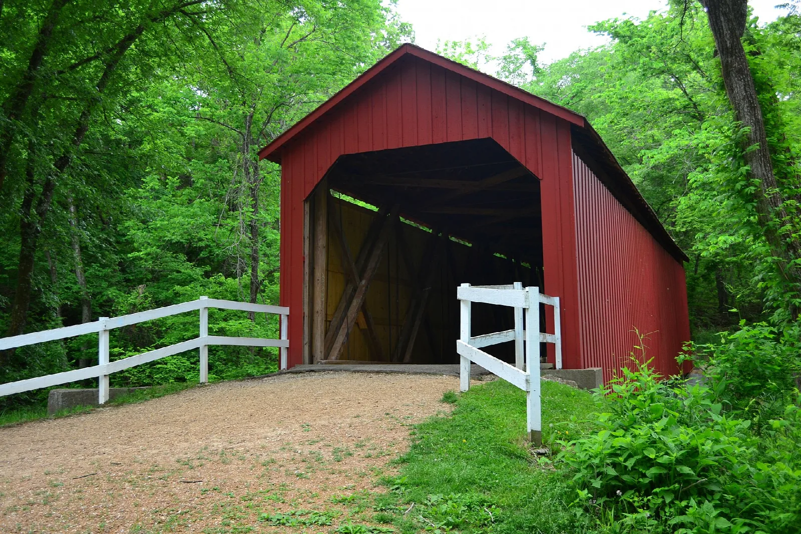 Red covered bridge with white fences and green trees