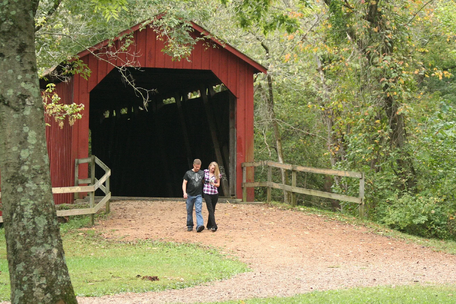 Red covered bridge entrance with two people walking on a gravel path