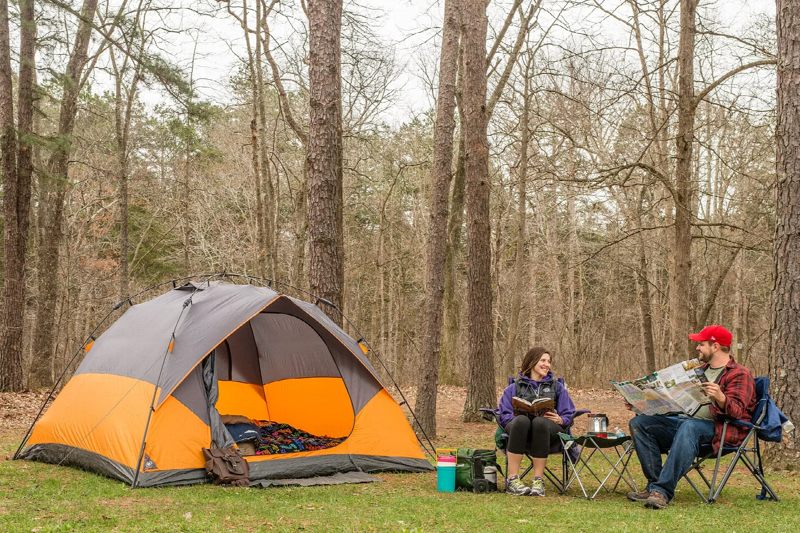 Orange tent in a grassy campsite among tall trees with two campers