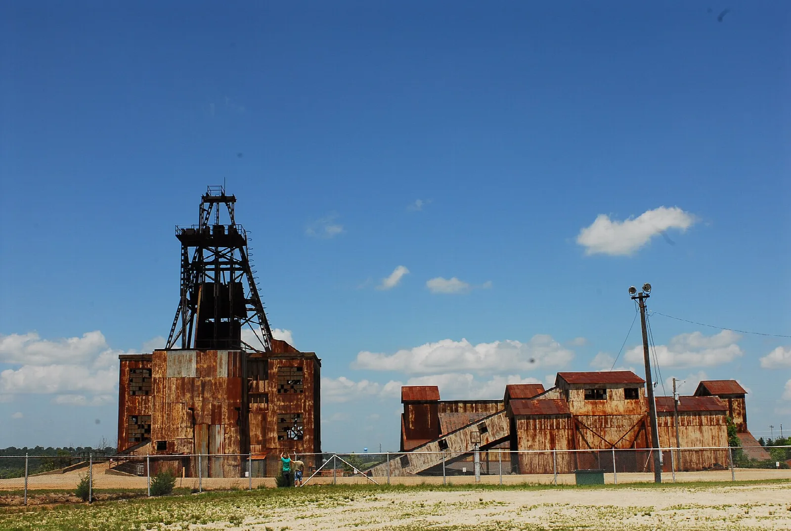 Rusty mill buildings and a headframe tower under a blue sky