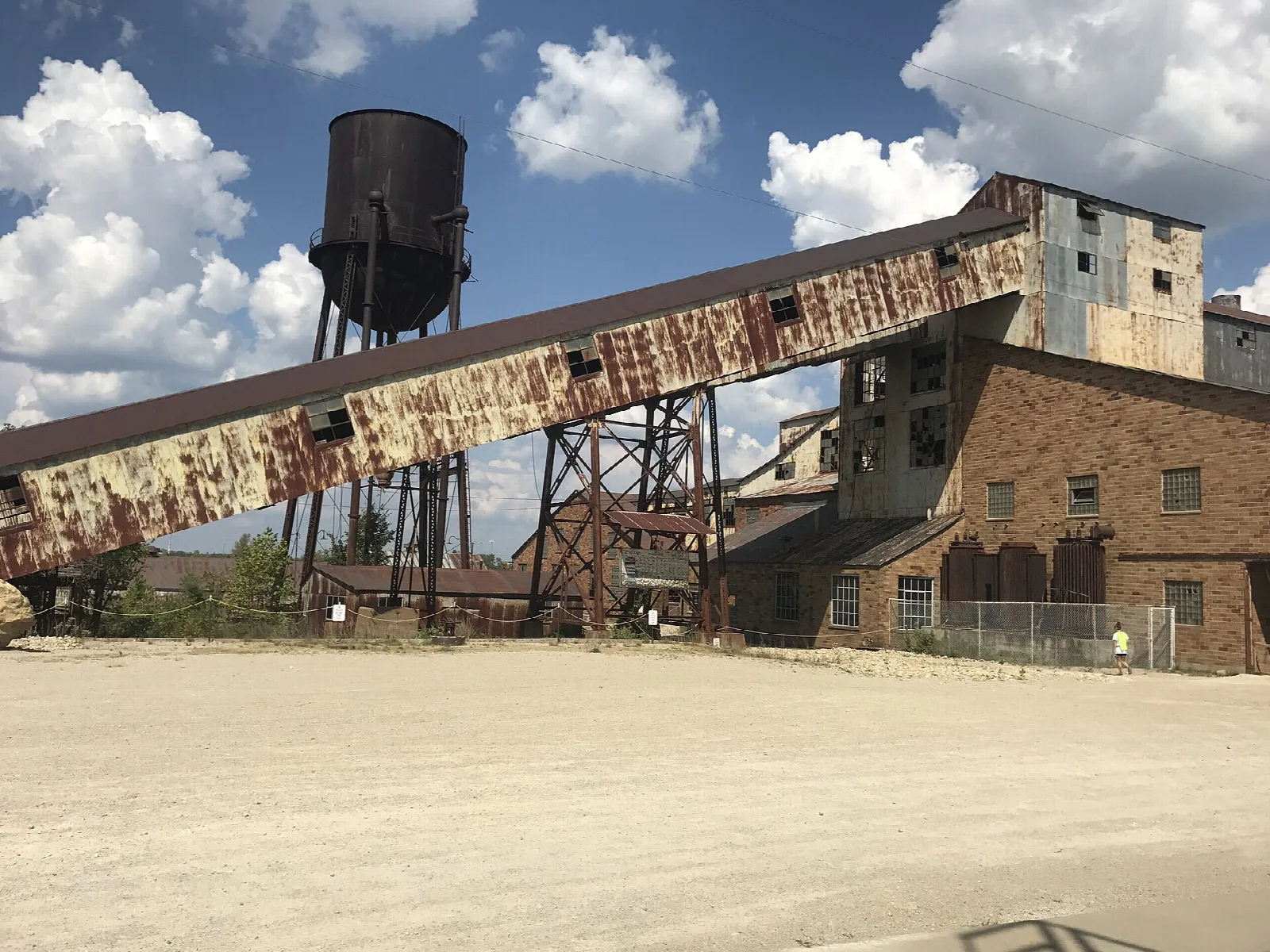 Long rusty conveyor leading to a brick mill with a water tower