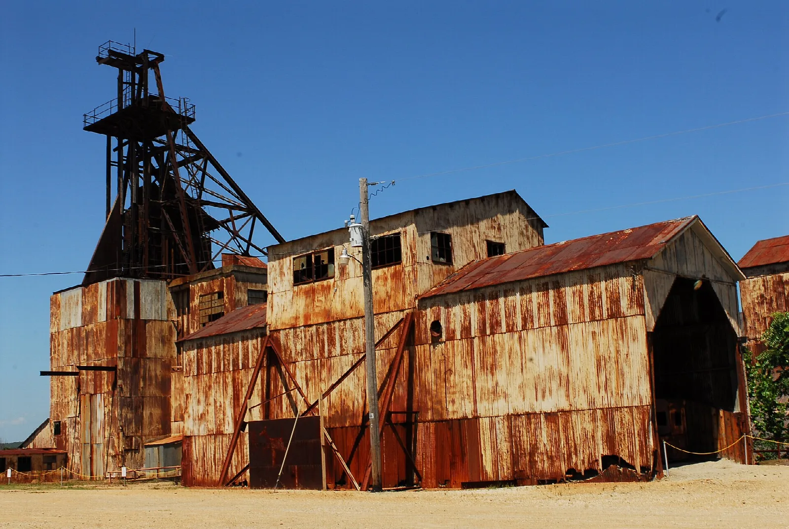 Rusty mill buildings with a tall headframe beside a gravel lot
