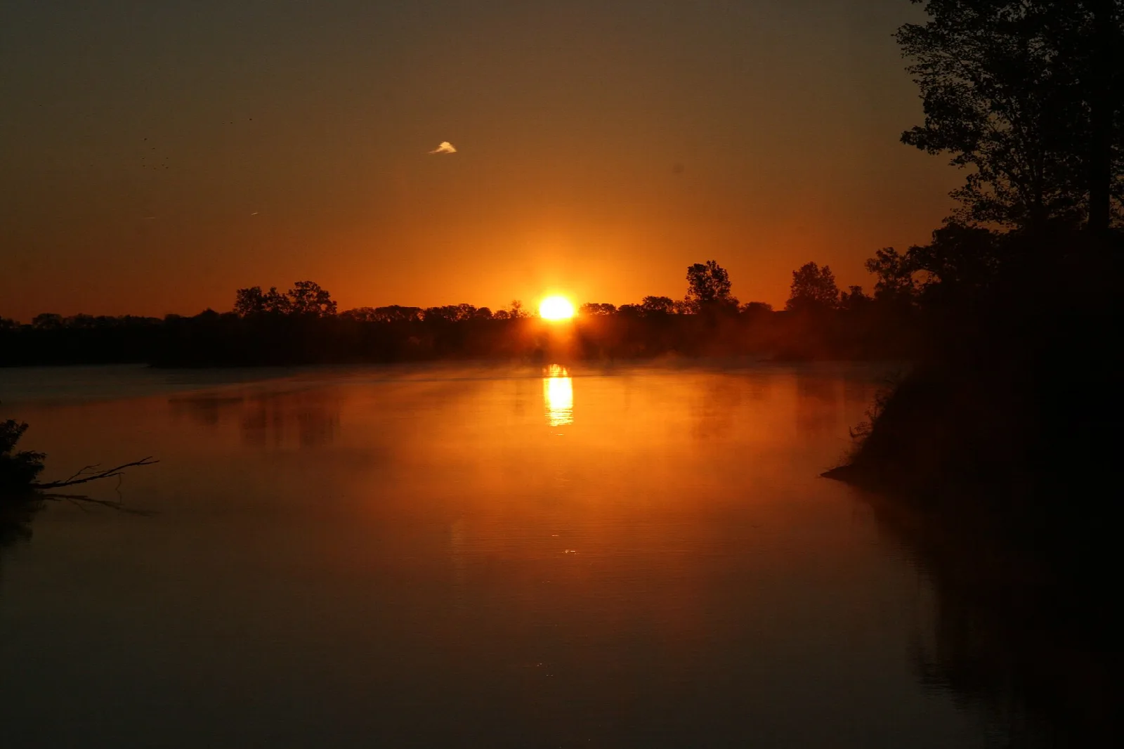 Sun setting over a calm lake with a dark tree line