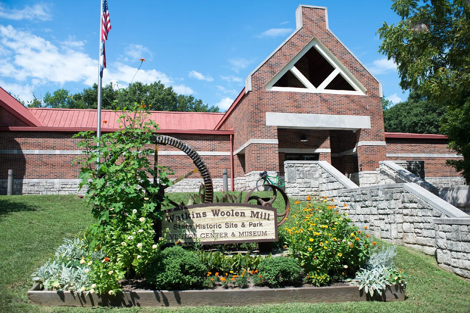 Brick building entrance with a flag and a flower bed in front