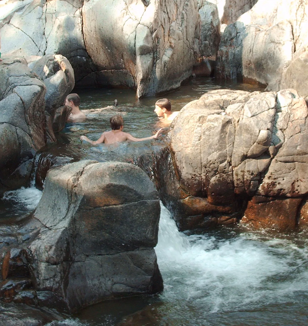Swimmers in a pool among smooth rounded rocks with a small waterfall