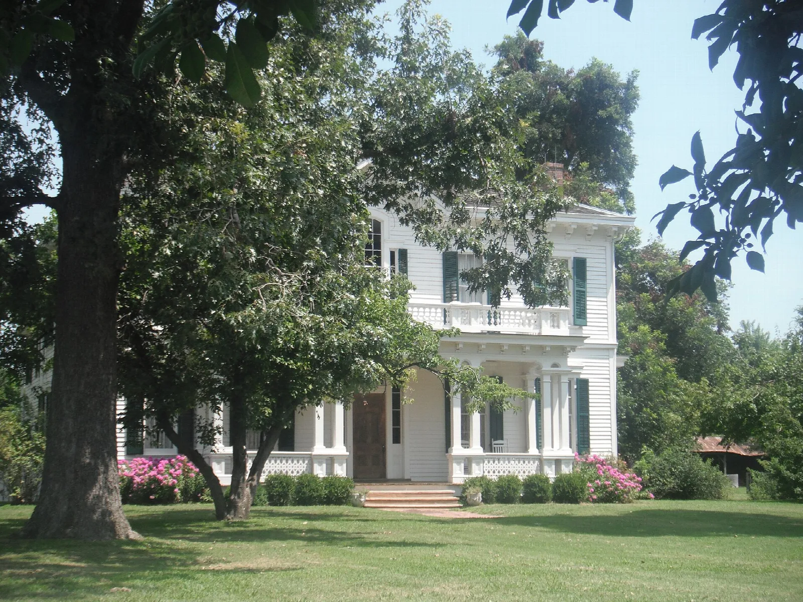 White historic house with a porch seen through trees across a green lawn