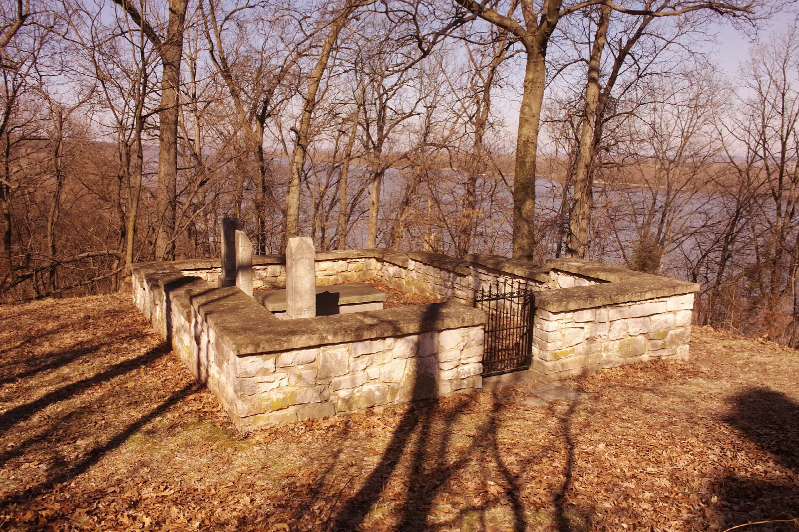 Stone-walled grave enclosure with small markers among bare trees and fallen leaves
