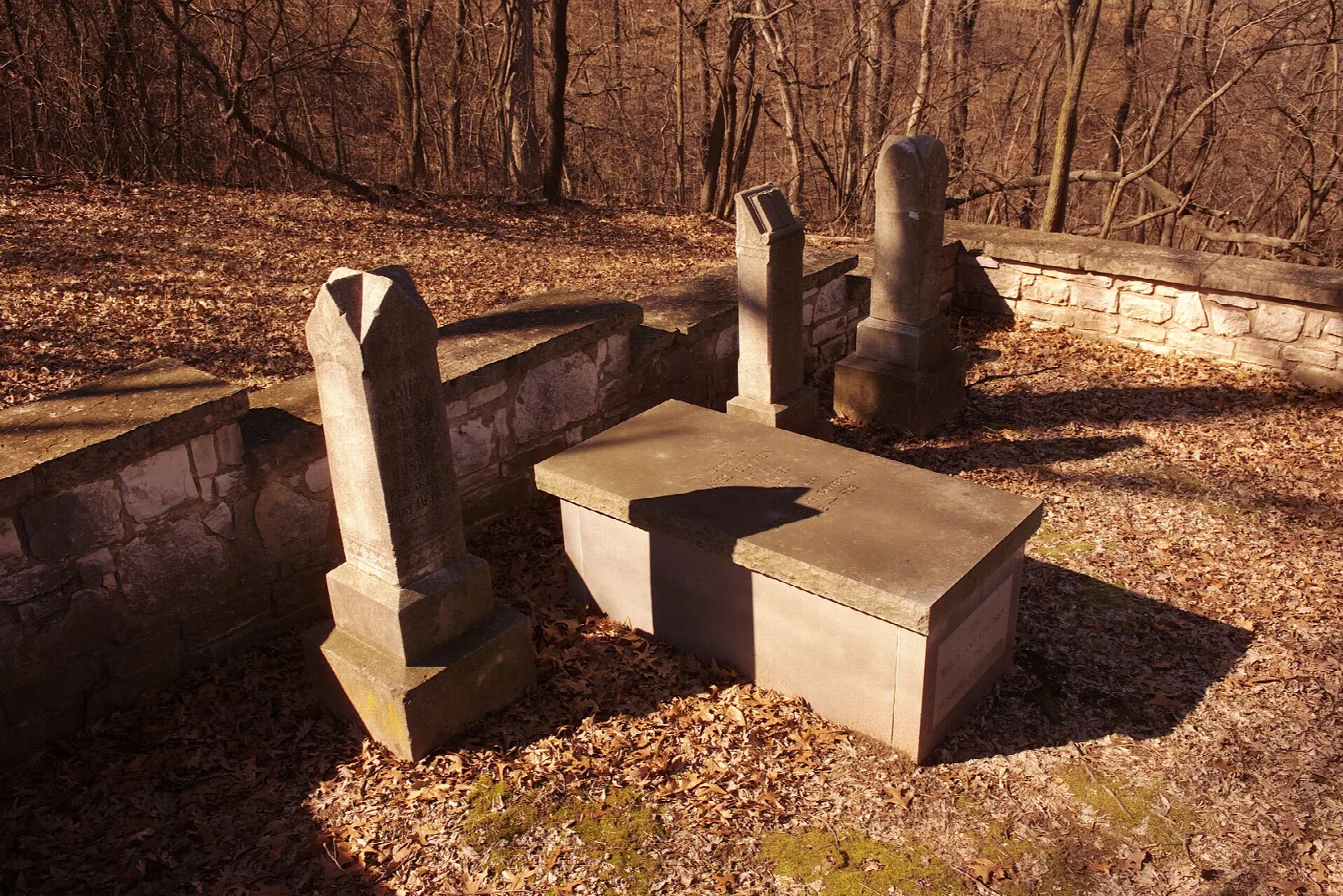 Stone grave markers and a flat slab inside a low stone wall, with fallen leaves
