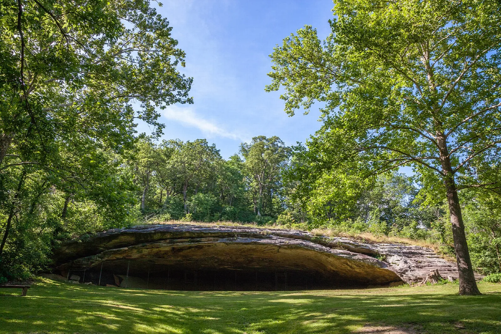 Wide sandstone shelter cave opening above a green lawn, framed by trees