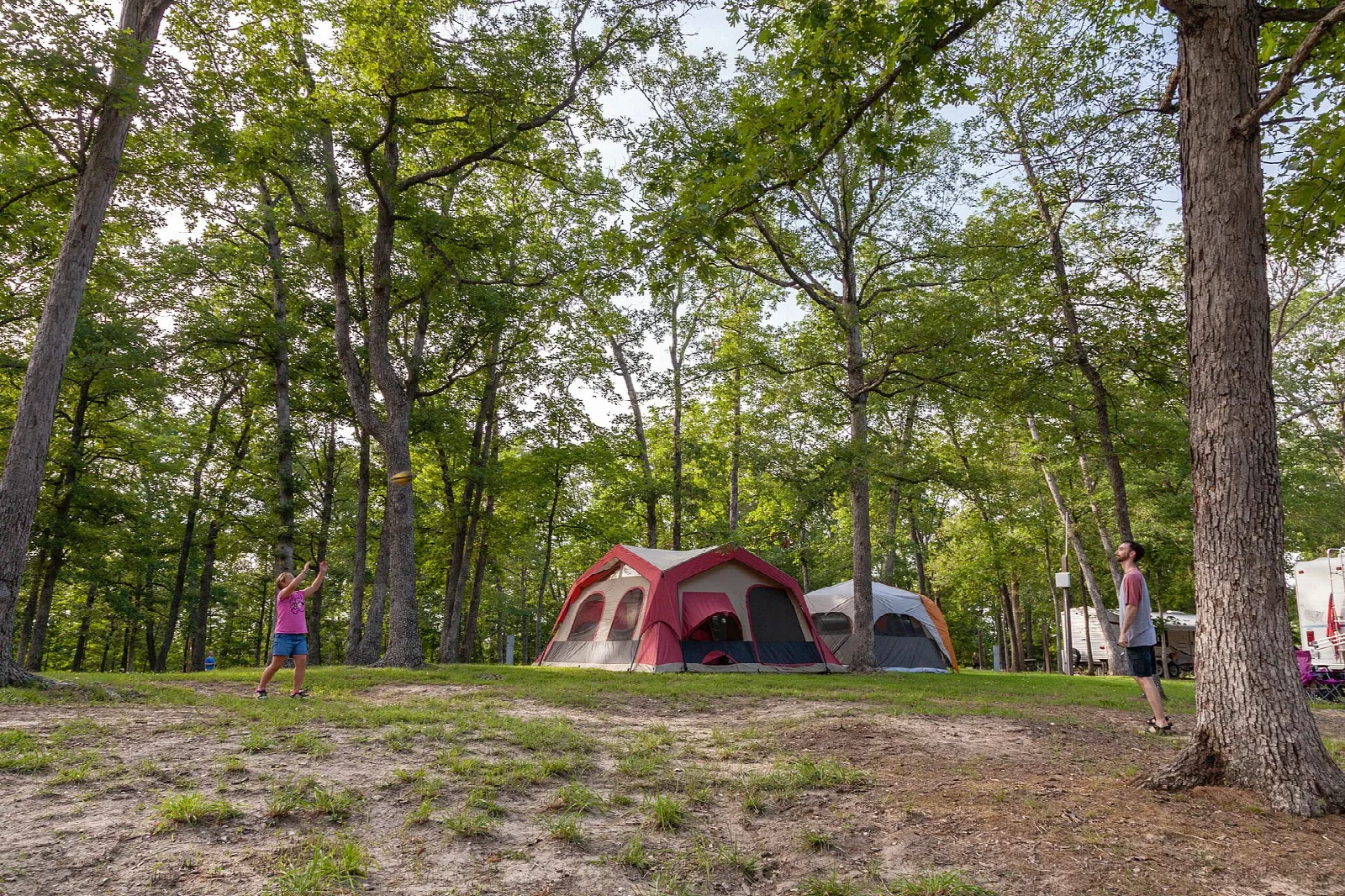 Two tents and two people in a shady wooded campsite clearing