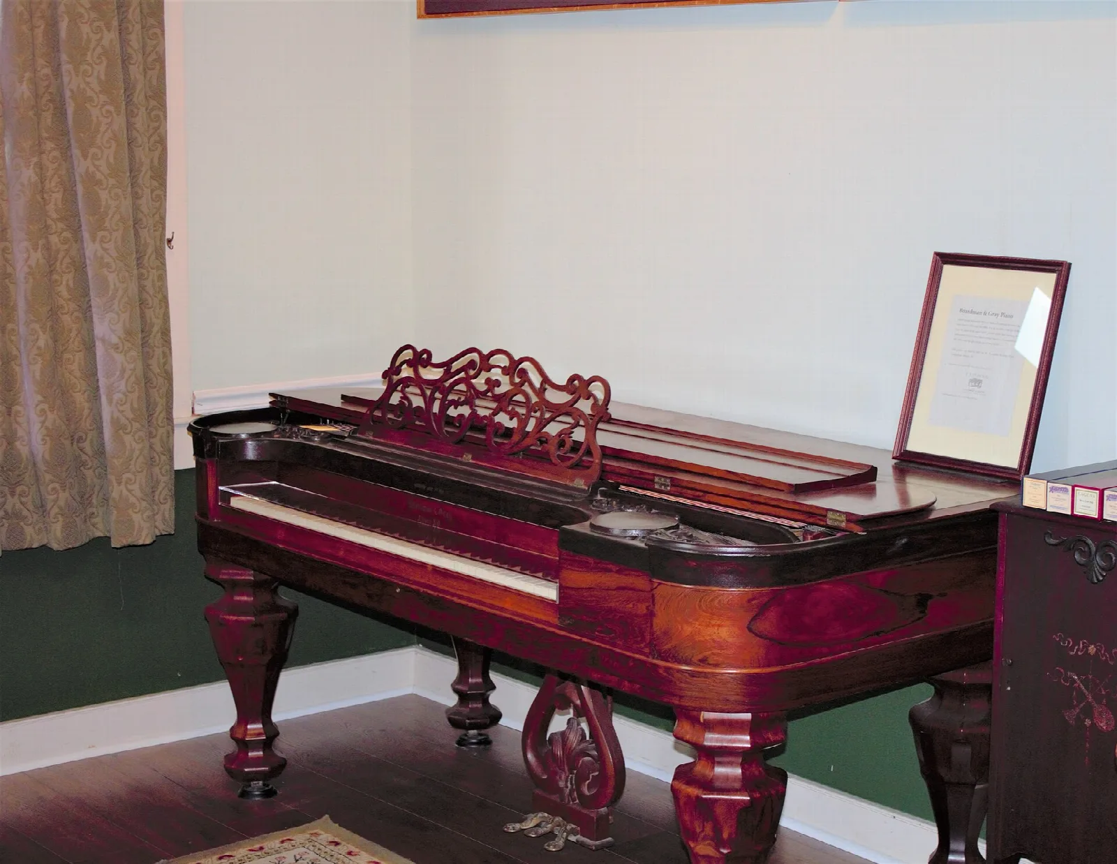 Antique square piano with a framed document in a plain room