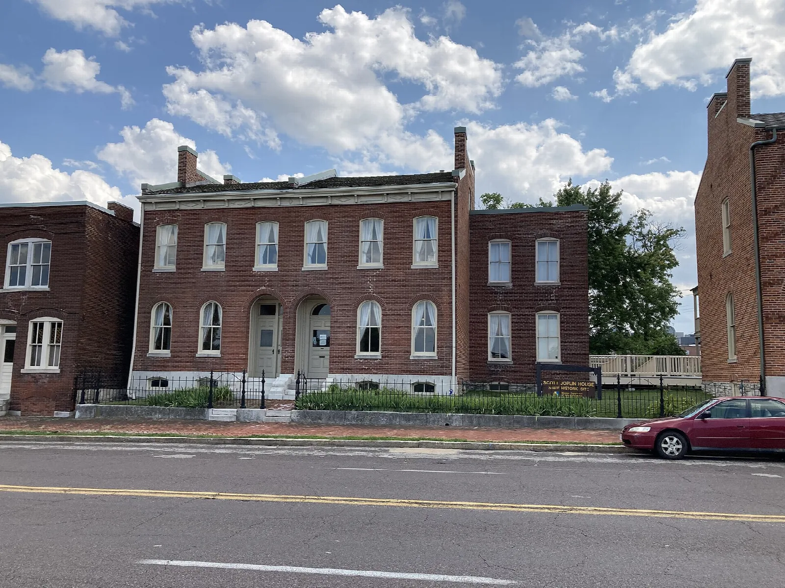 Red brick row houses on a street under a blue sky with clouds