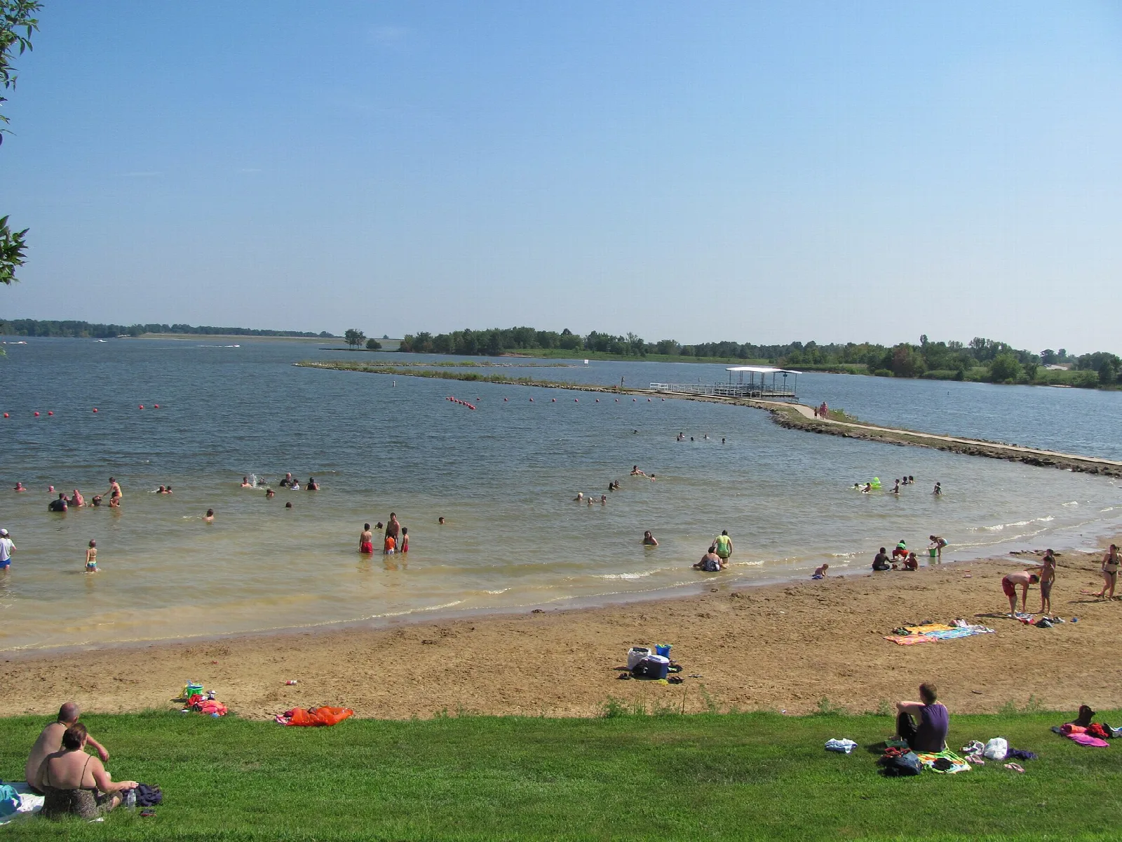 Swimmers and sunbathers on a sandy beach along a wide lake