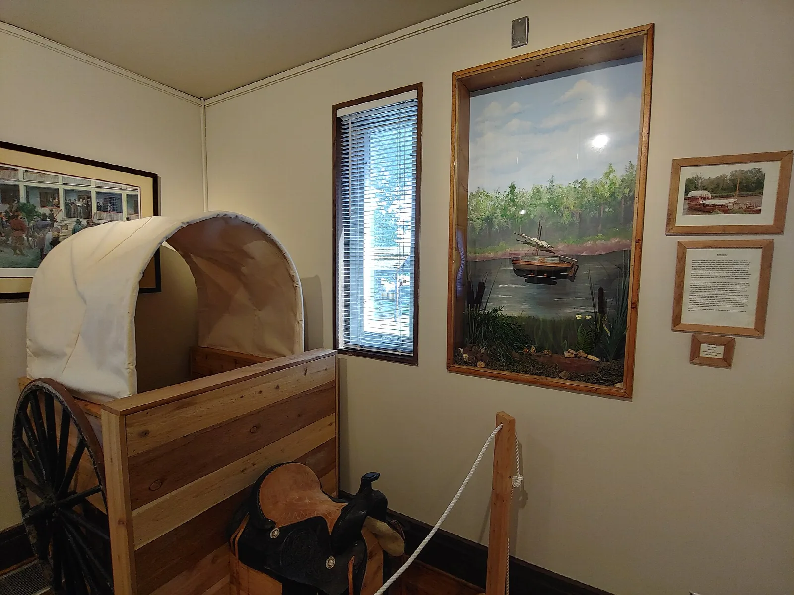 Museum room with a covered wagon model, saddle and framed painting