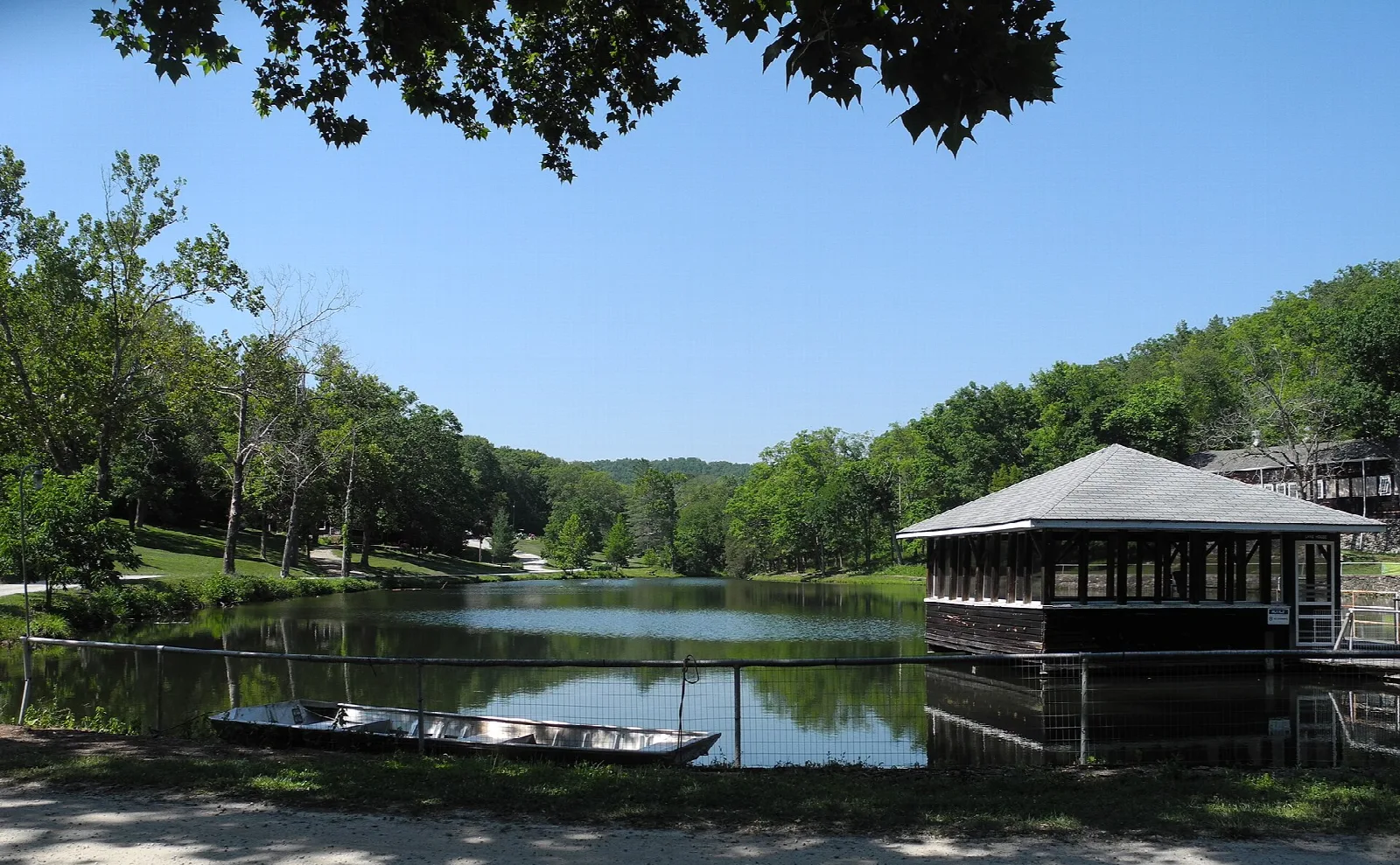Pond with a small boat and an open lake house under blue sky