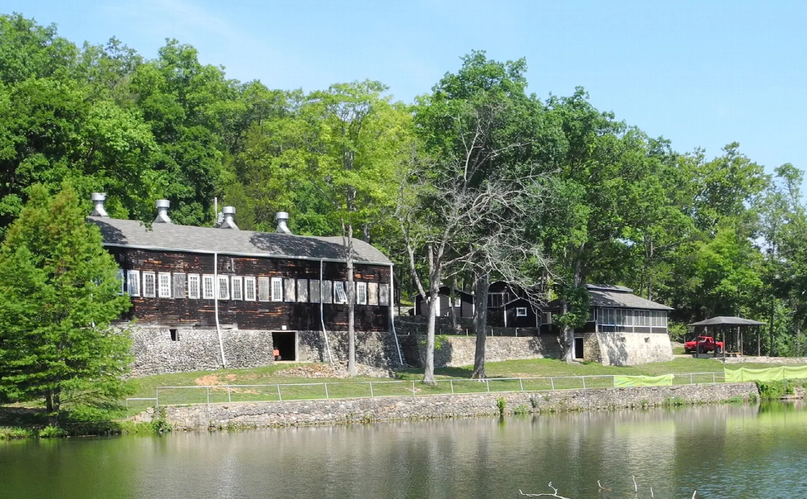 Rustic dark wood lodge buildings beside a pond, framed by green trees