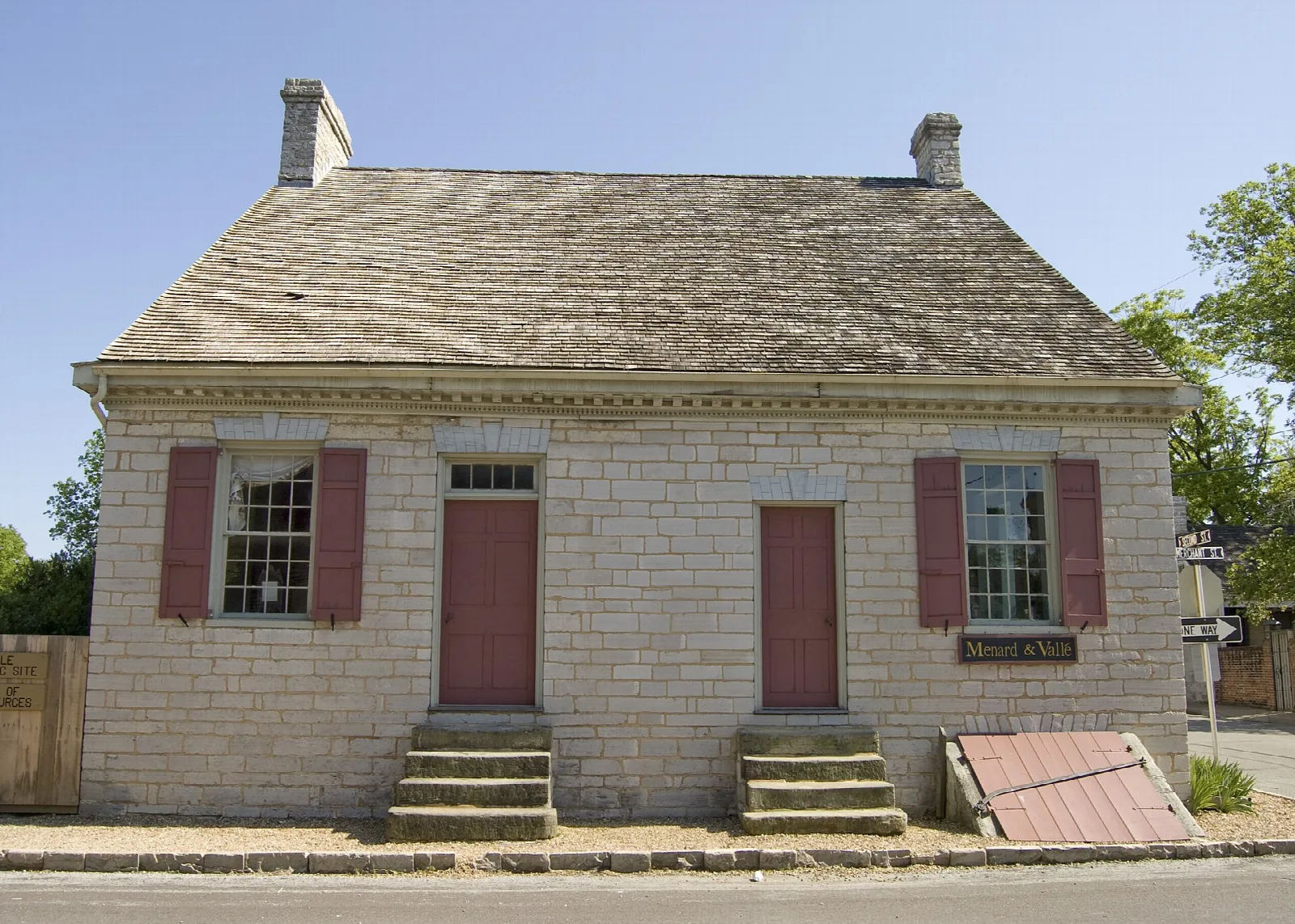 Front of a stone house with red shutters and a low gabled roof