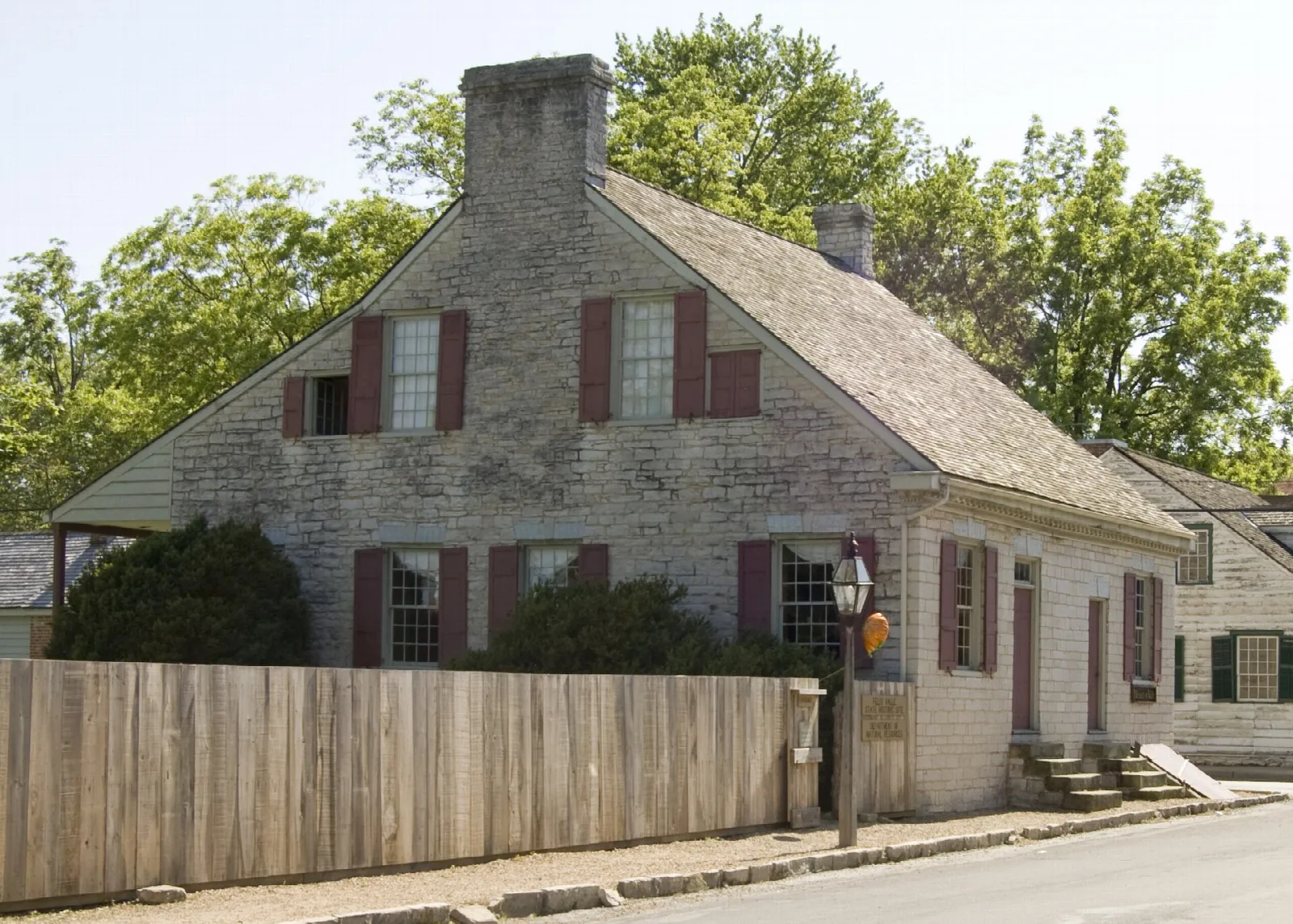 Stone house with a steep roof behind a wooden fence