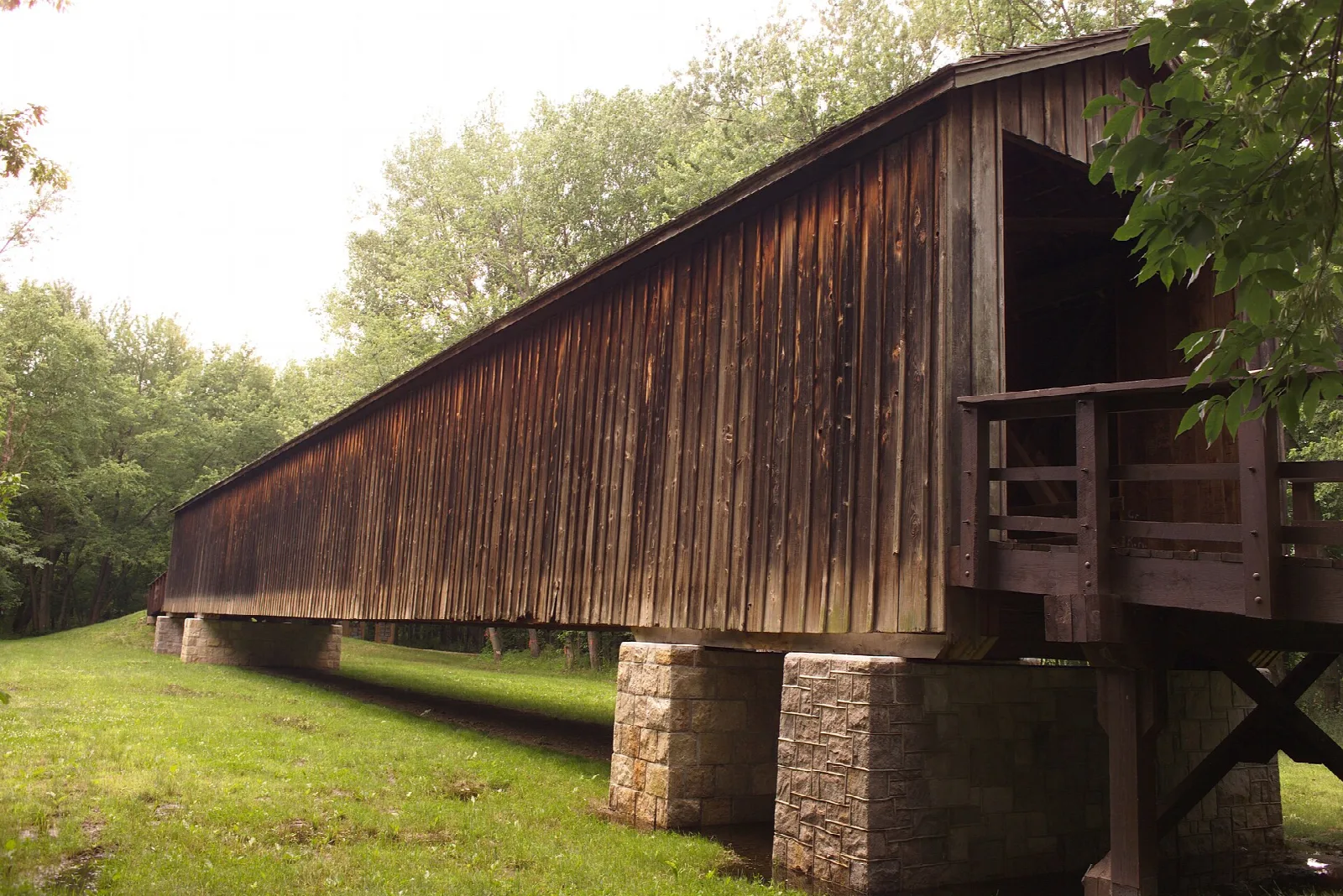 Long dark wooden covered bridge on stone piers beside a grass field