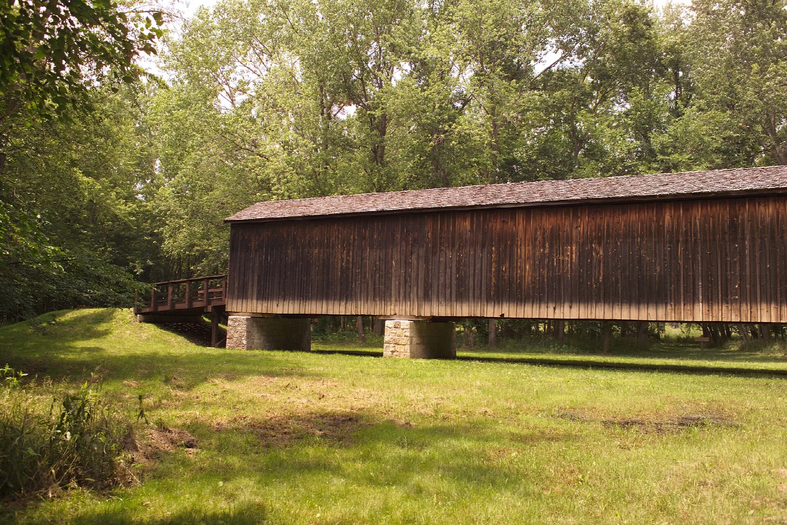 Side of a wooden covered bridge across a green clearing