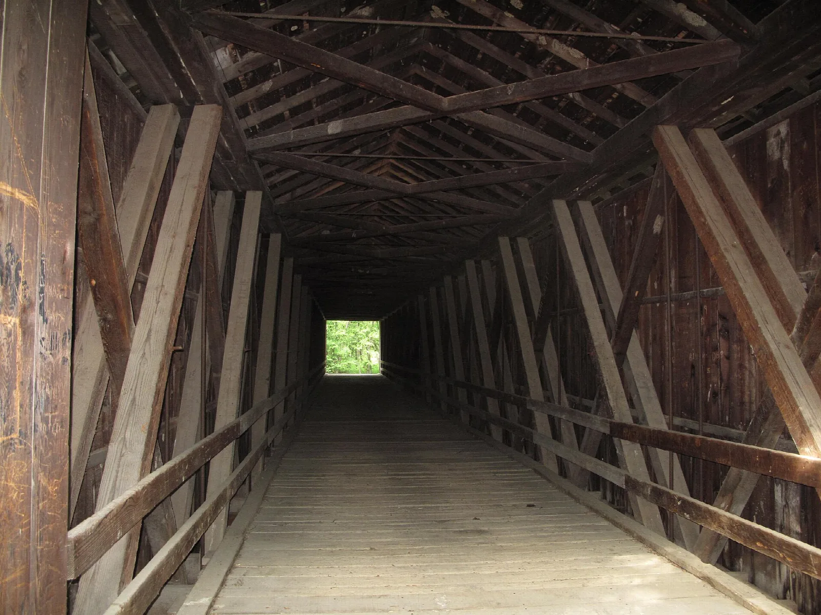 Inside a covered bridge, timber framing leading to a bright opening
