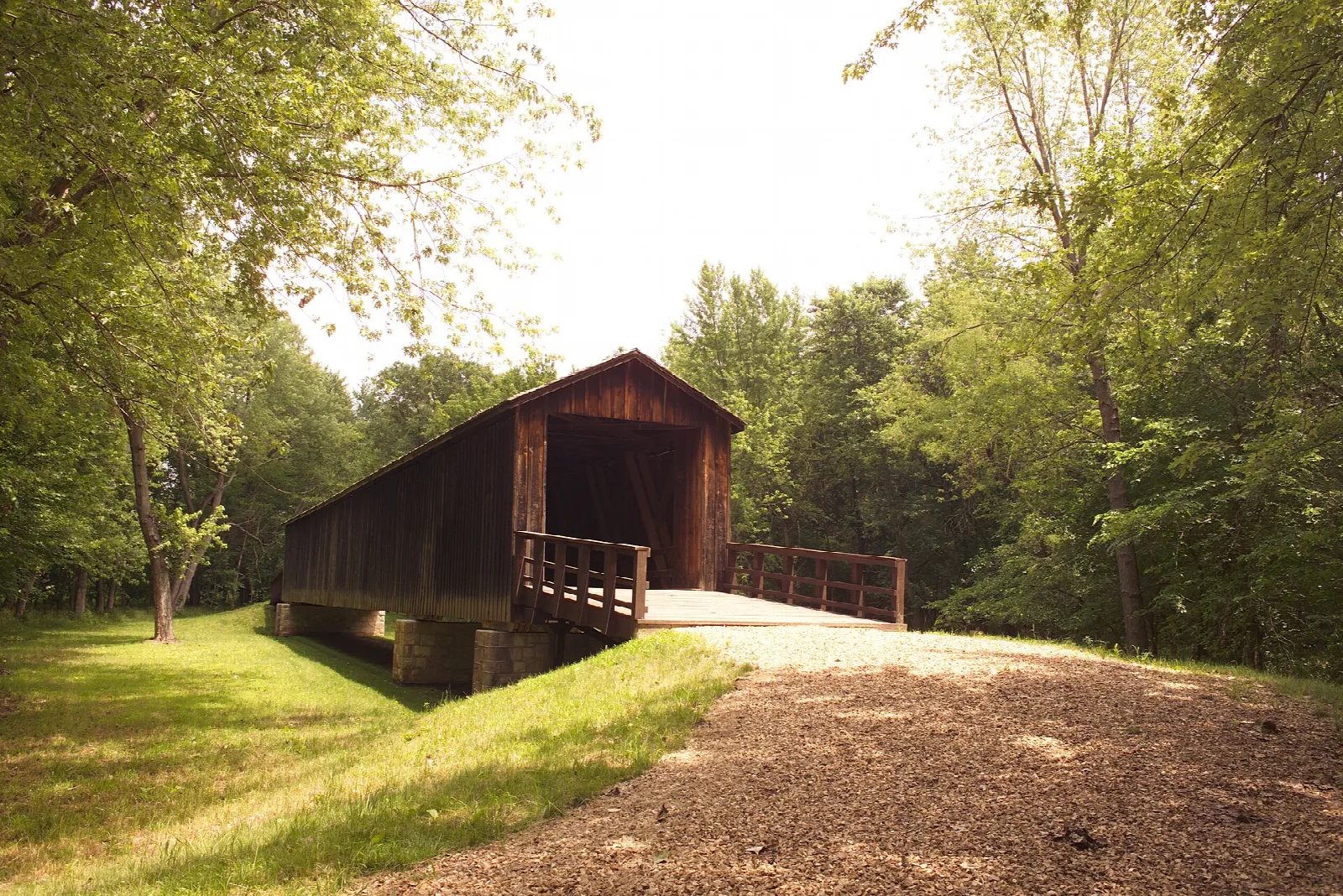 Covered bridge entrance with a gravel path and trees