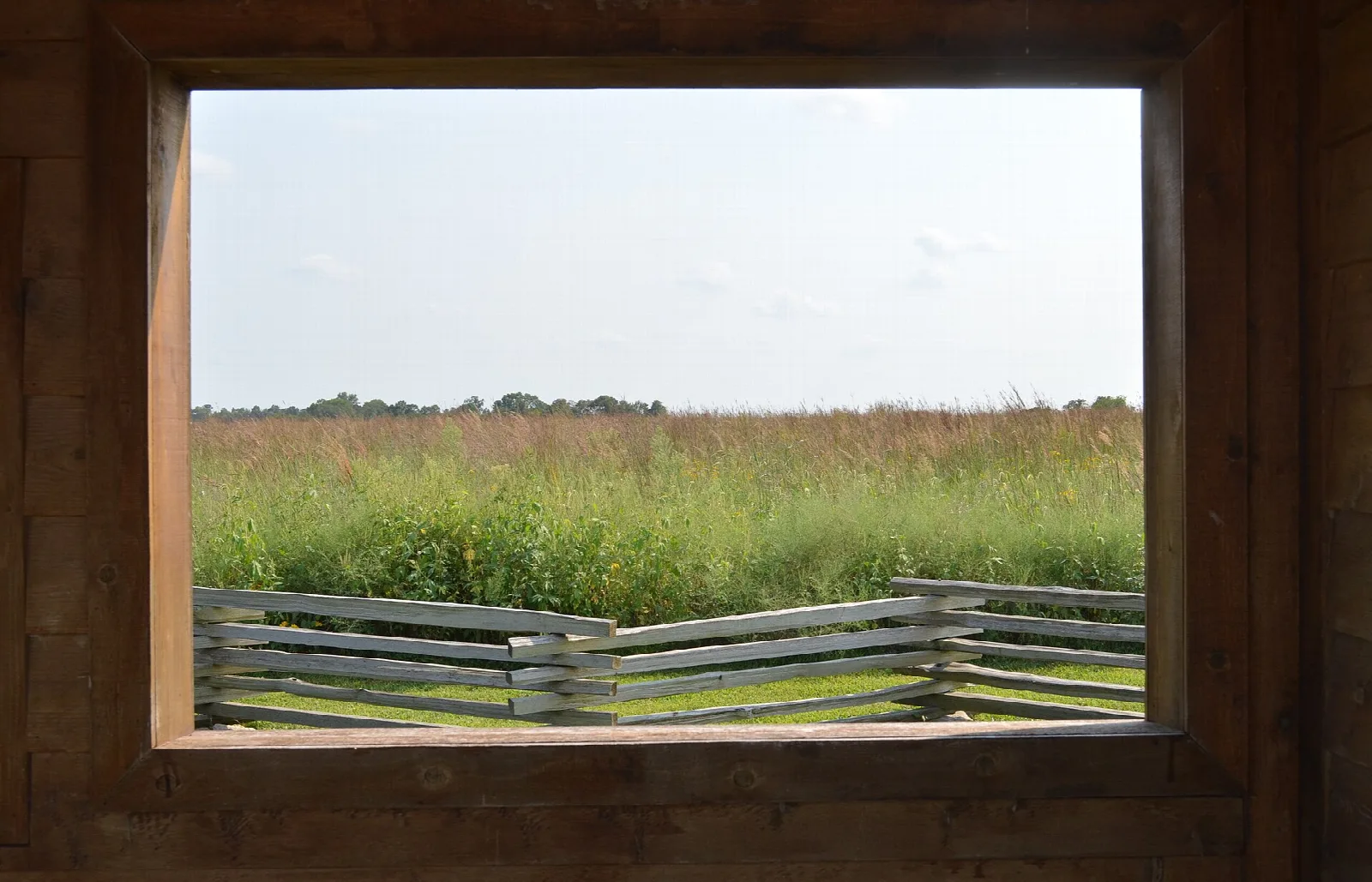 View through a wooden window frame over prairie grass and a split-rail fence