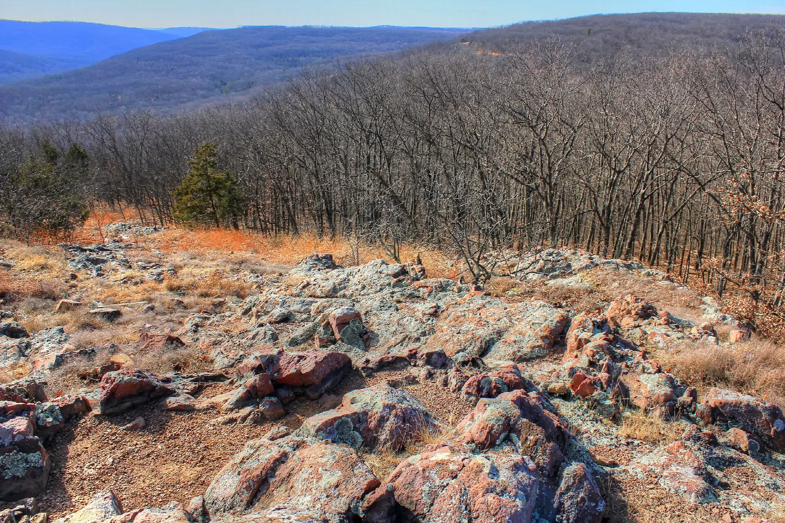Pink and gray rocks on a ridge with bare winter forest and distant hills