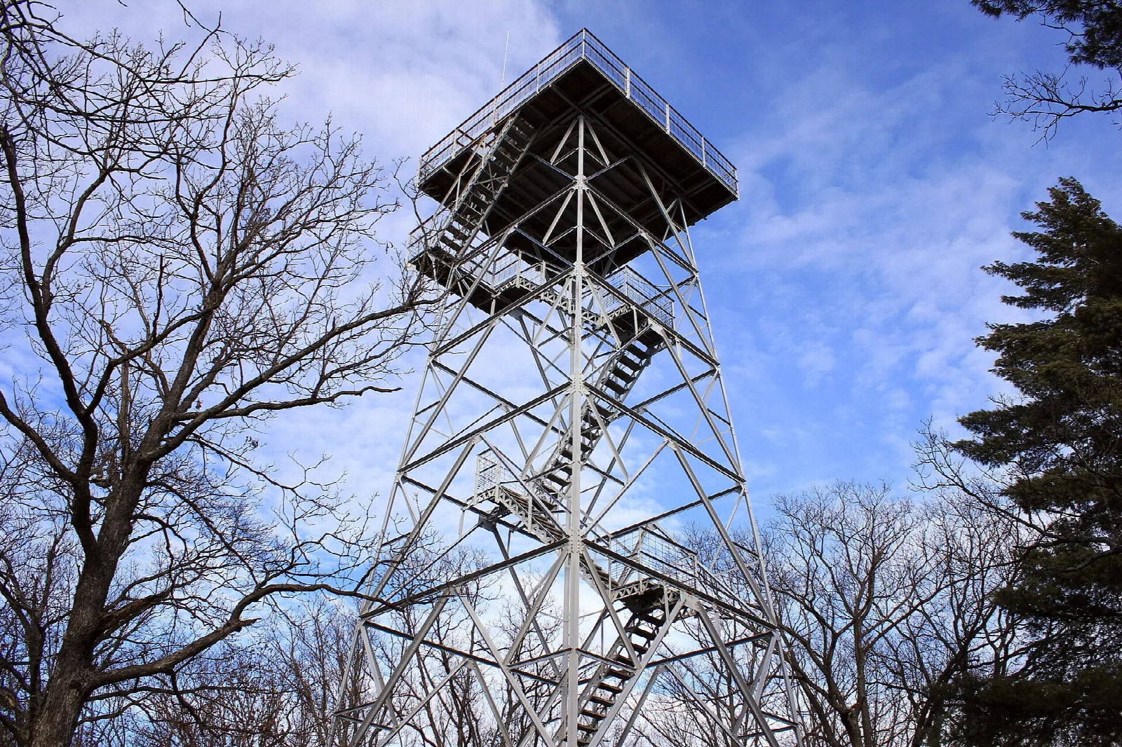 Steel fire-tower-style watchtower against a blue sky with bare trees