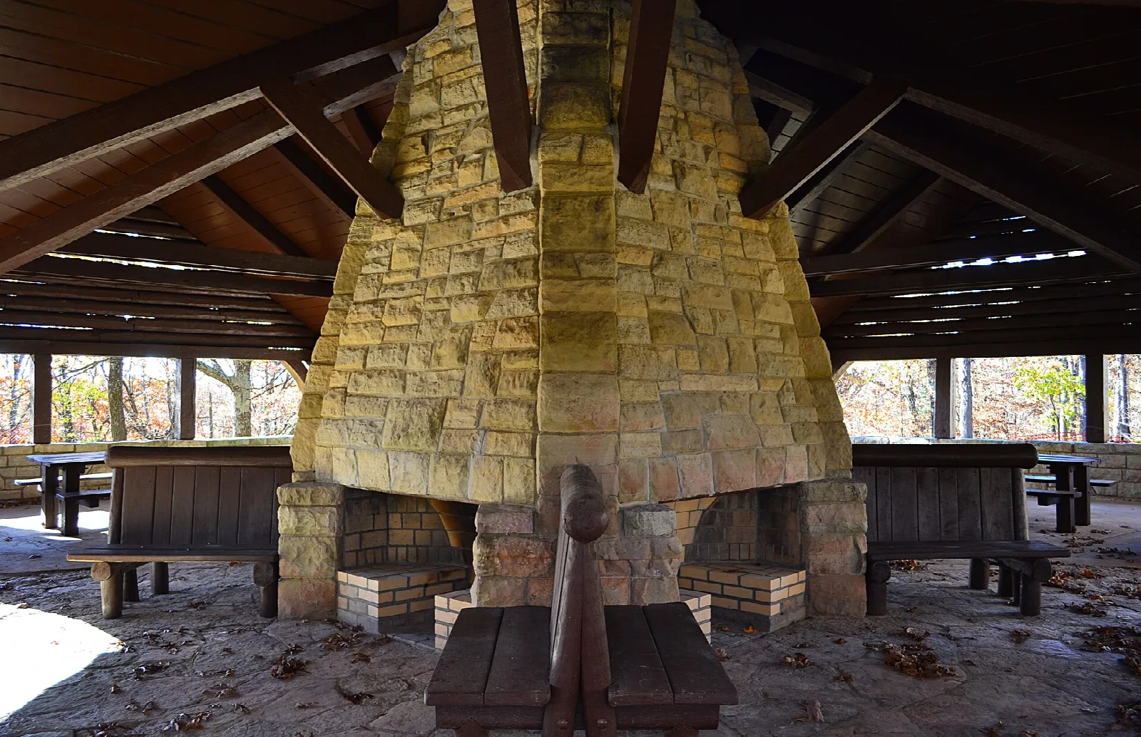 Stone picnic shelter with a big fireplace and wooden tables