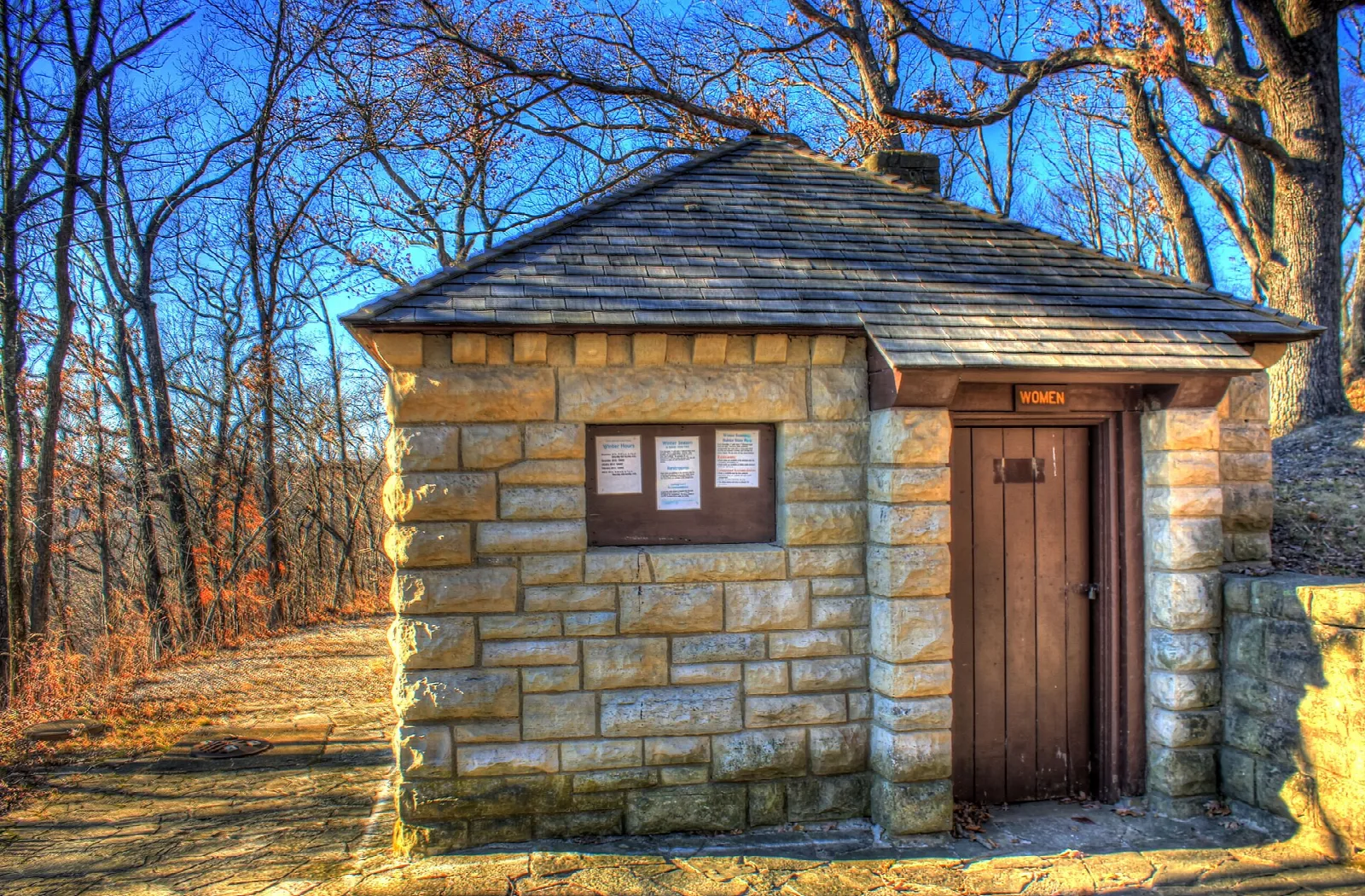 Small stone building with a shingled roof beside a path in winter woods